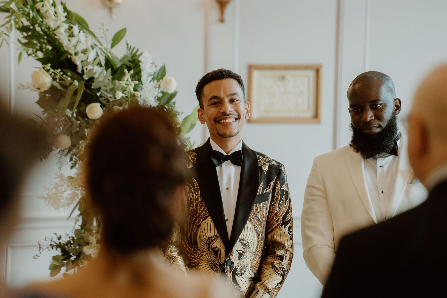Groom smiling joyfully at the altar in a gold embroidered tuxedo jacket during wedding ceremony.