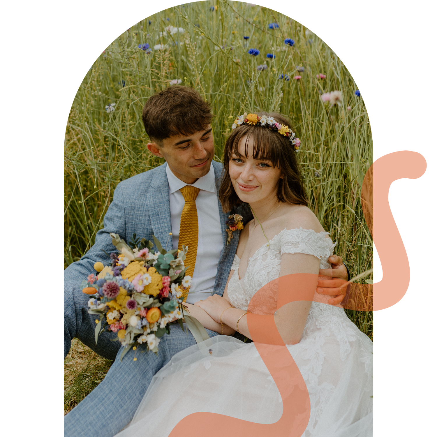 Romantic couple sitting in wildflower meadow, bride in floral crown with colorful bouquet, groom in light blue suit.