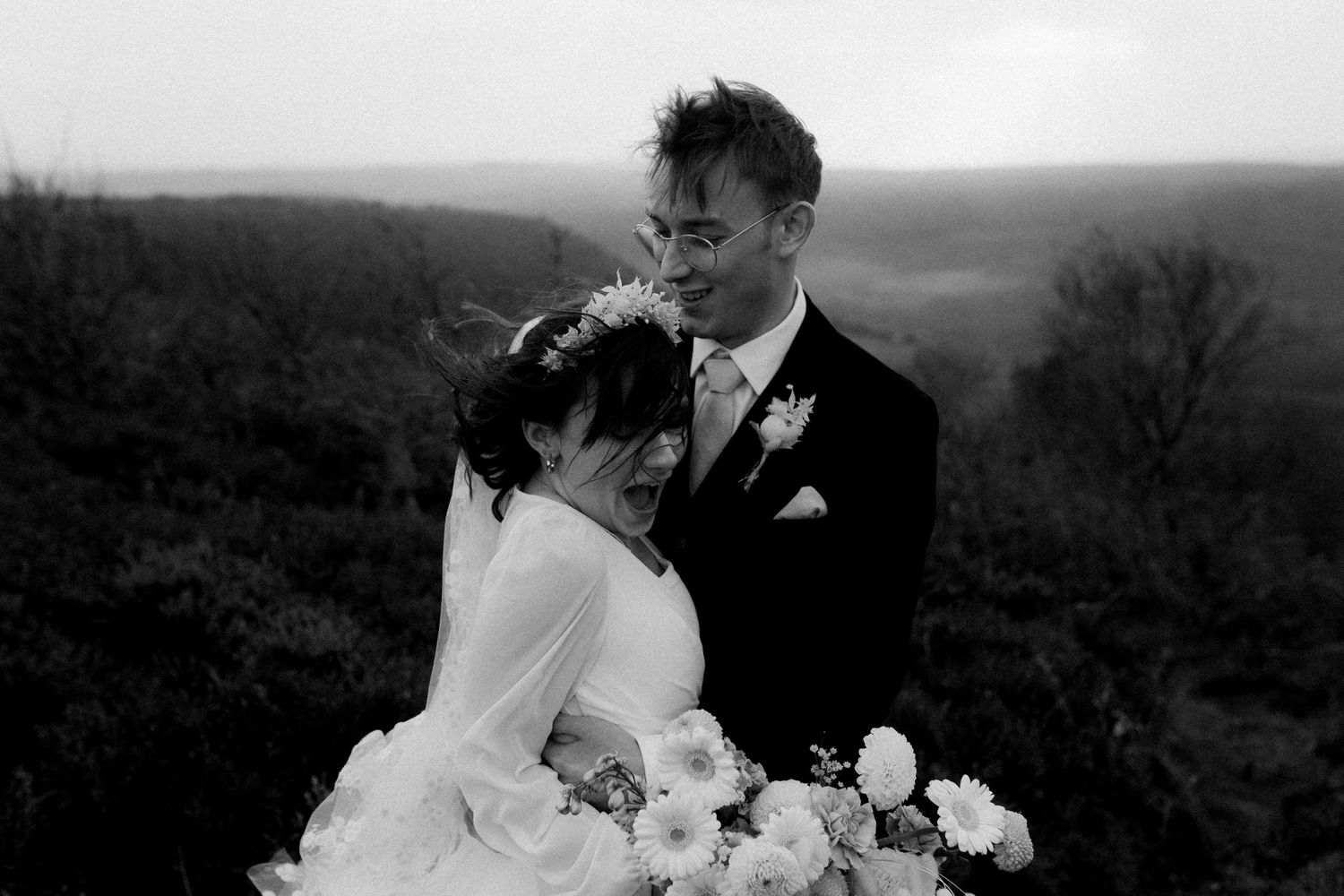 Black and white wedding portrait capturing a tender moment against rolling hills.