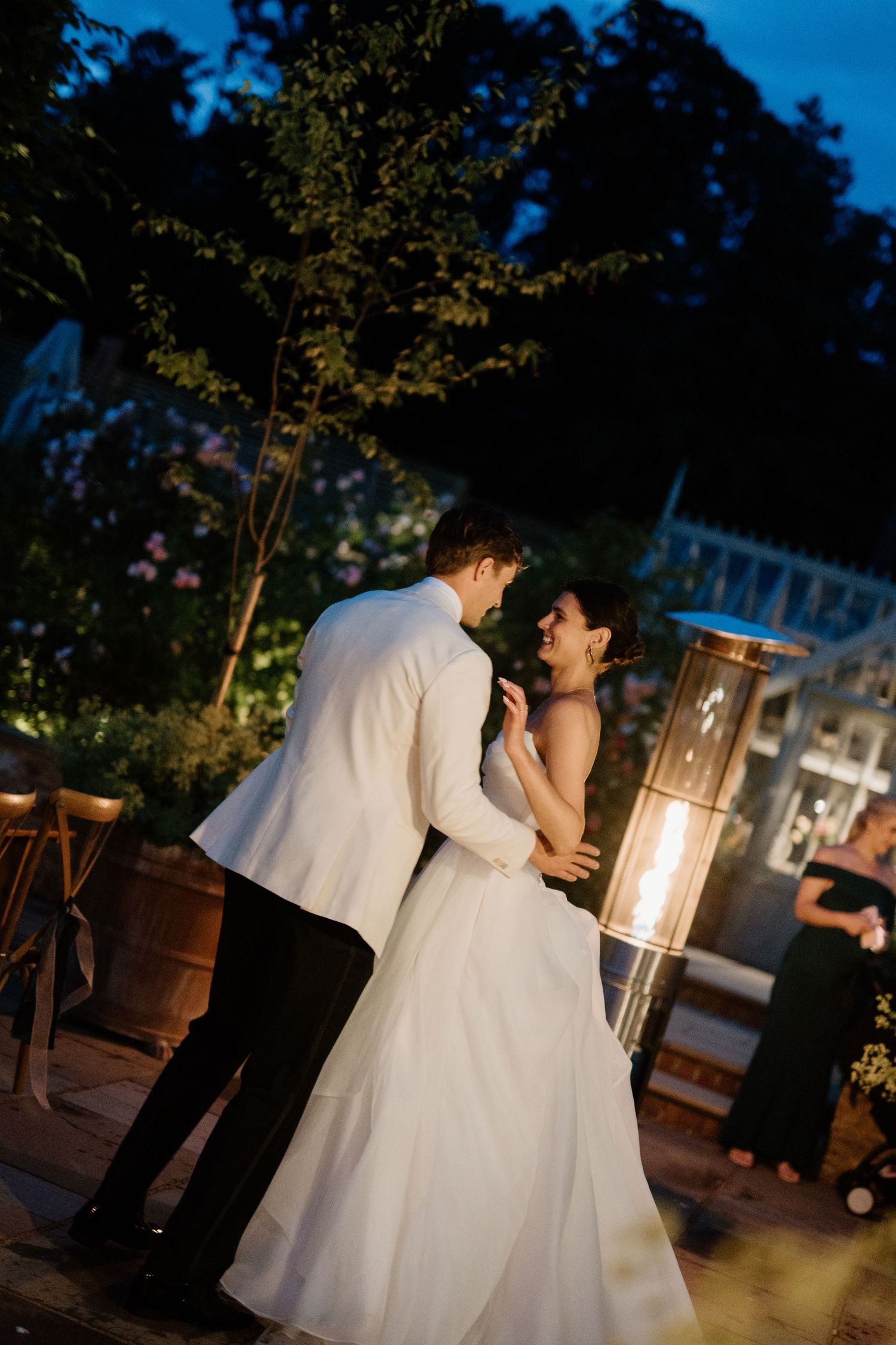Bride and groom laughing during outdoor evening first dance by fire torch.