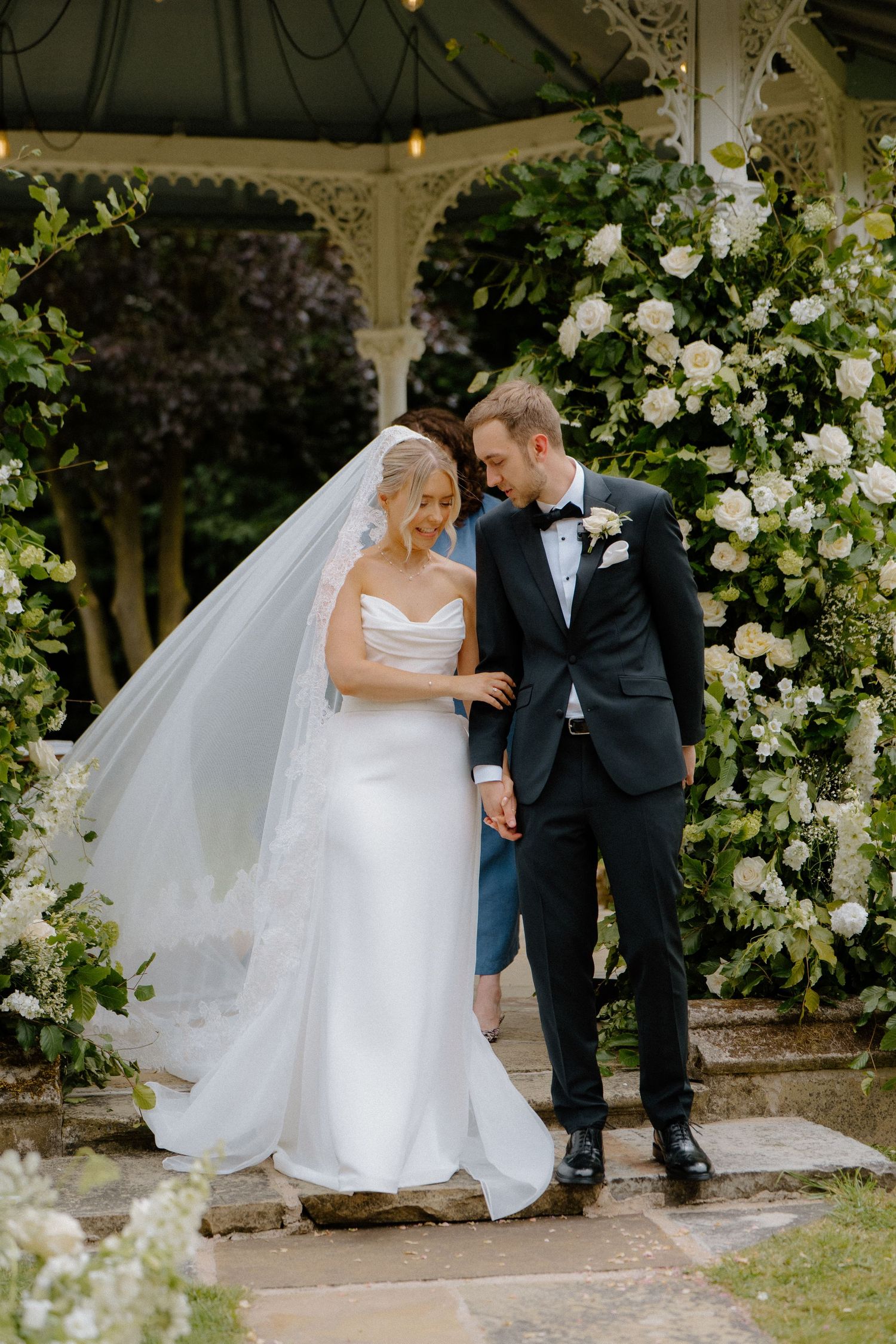 Bride and groom standing together under a white gazebo adorned with white floral arrangements at their wedding.
