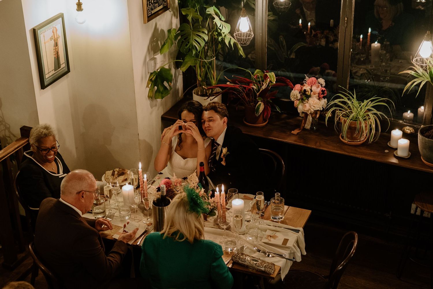 Bride and groom laughing together at their candlelit wedding reception table surrounded by guests.