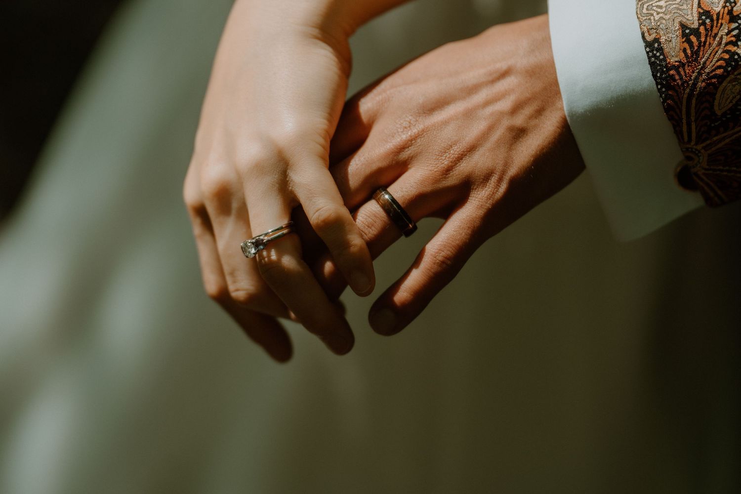 Close-up of bride and groom holding hands showing their wedding rings, batik sleeve visible.