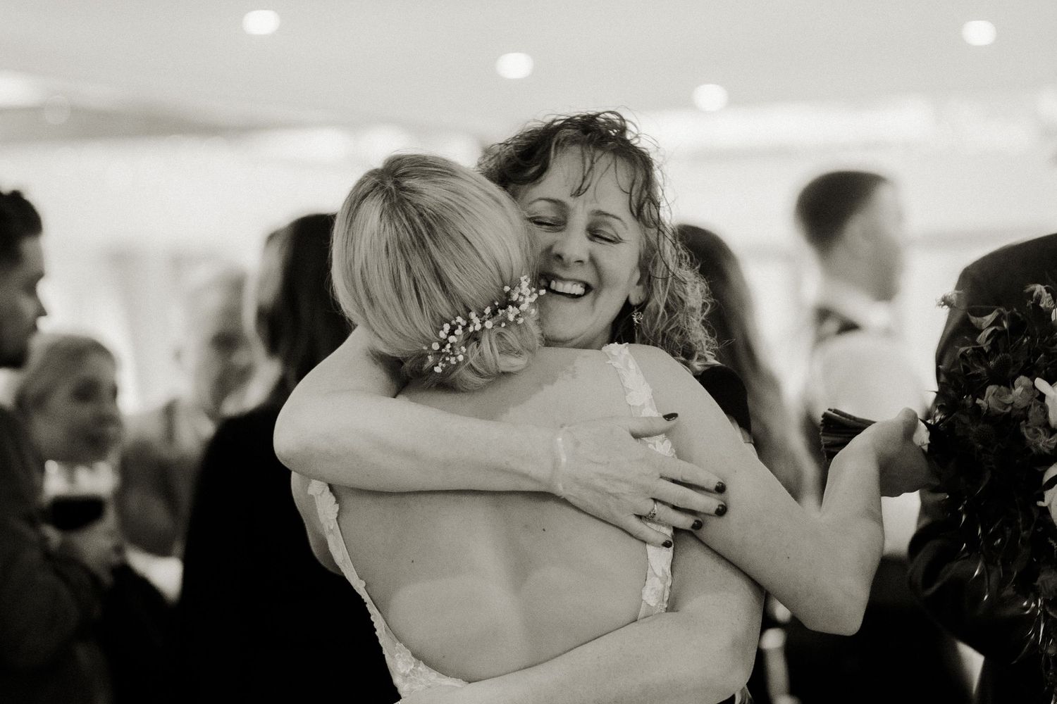 Black and white photo of two women sharing a heartfelt hug at a wedding reception celebration.
