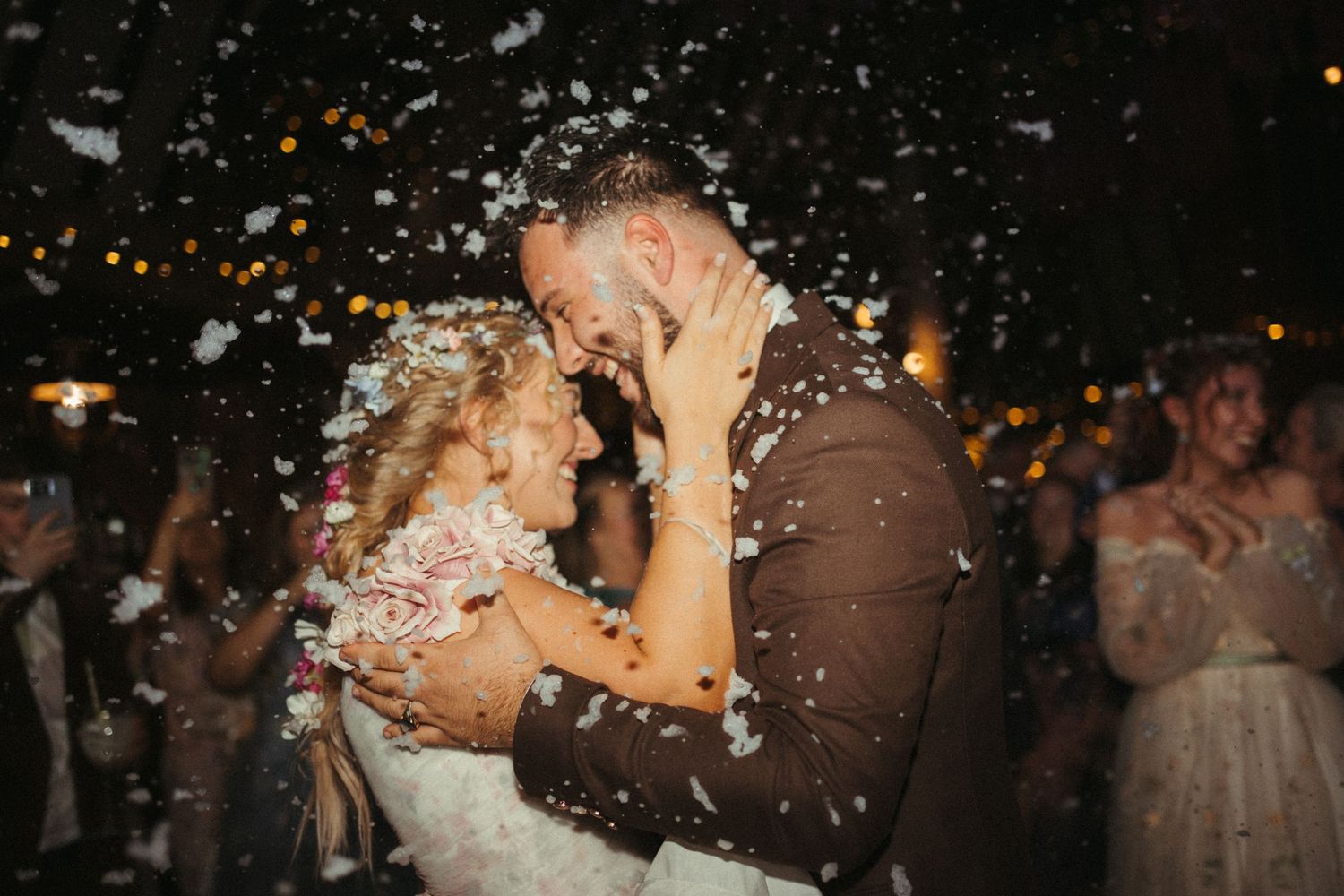 Bride and groom share a romantic kiss surrounded by falling confetti during their wedding celebration.