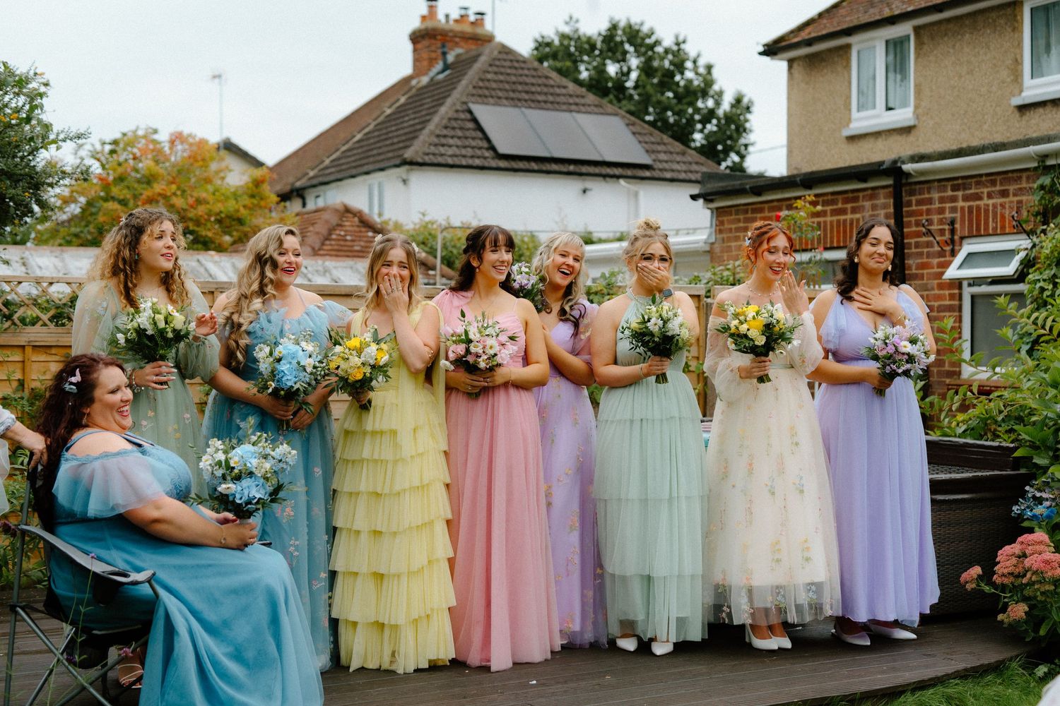 Seven bridesmaids in colorful pastel rainbow tulle dresses holding bouquets at outdoor wedding.