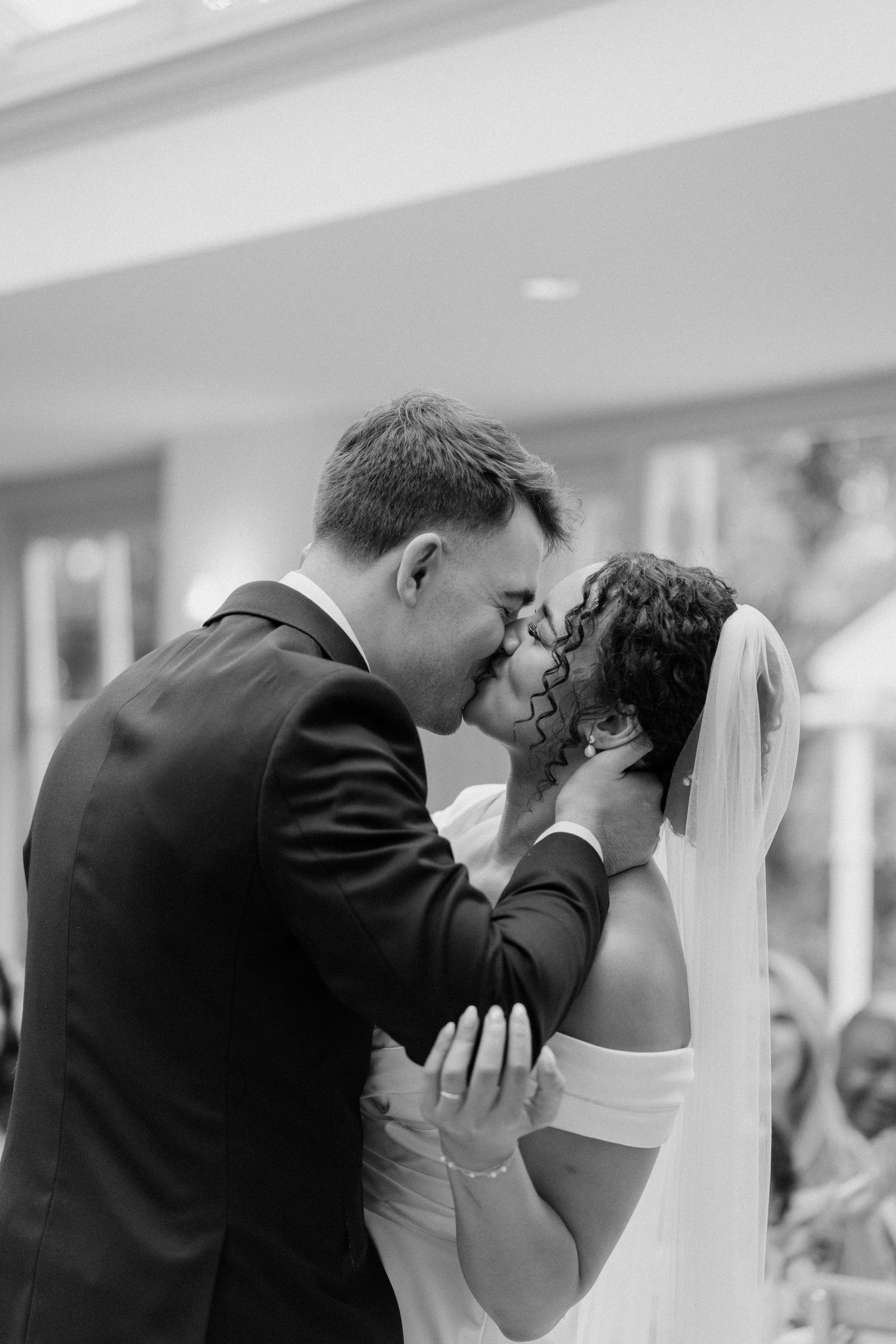 Bride and groom sharing first kiss in black and white wedding photo.