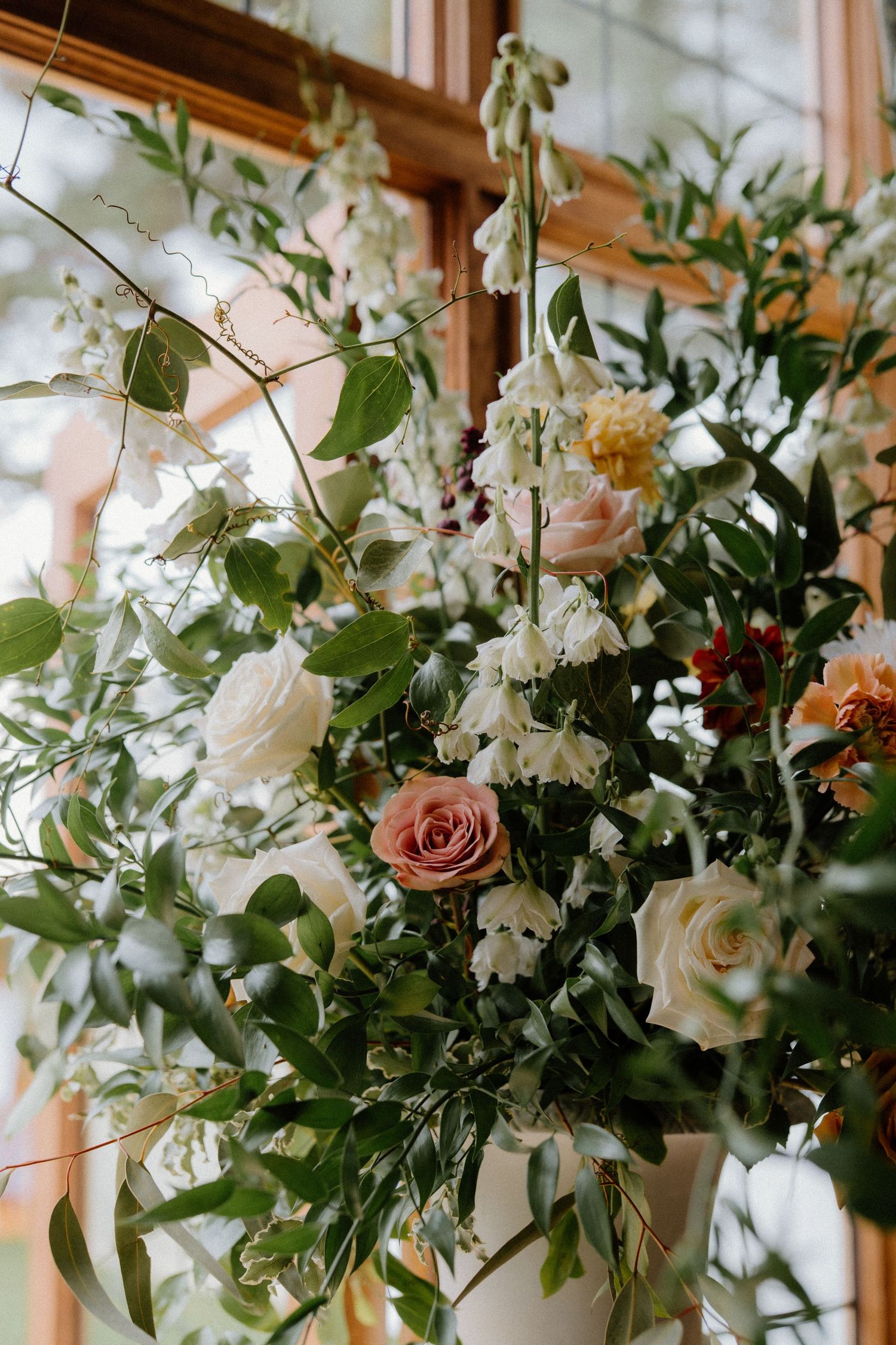 Lush wedding floral arrangement of white and pink roses with greenery near window.