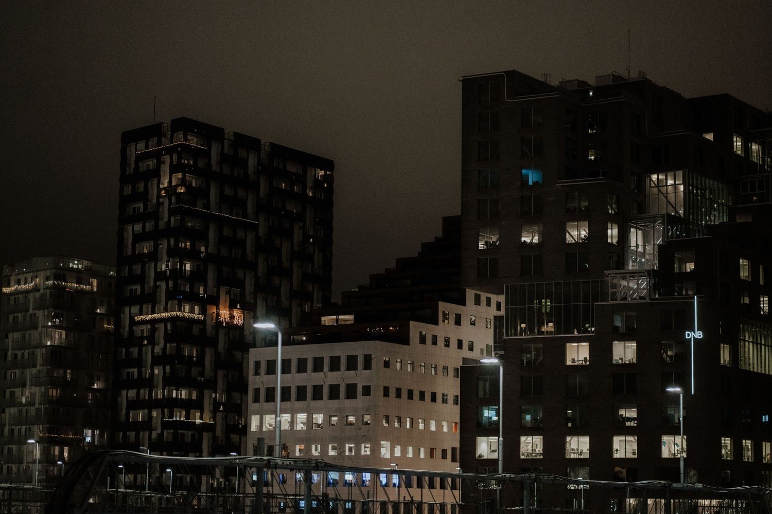 Dark city buildings at night with scattered illuminated windows creating an moody urban landscape.