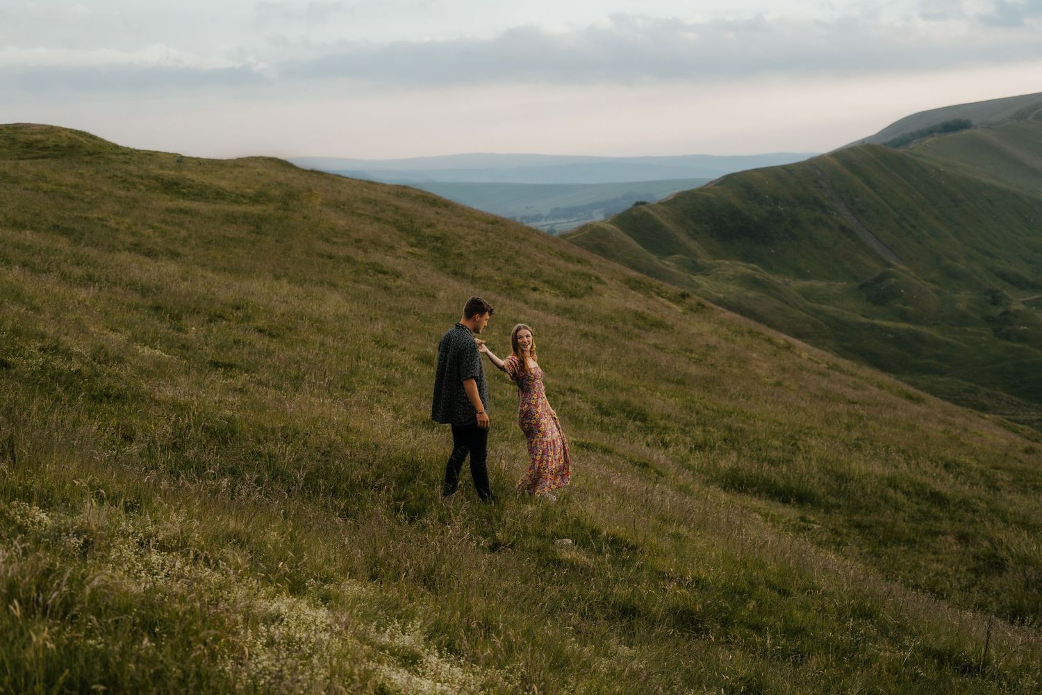 Couple walking hand in hand through lush green highland hills during a romantic outdoor engagement shoot.