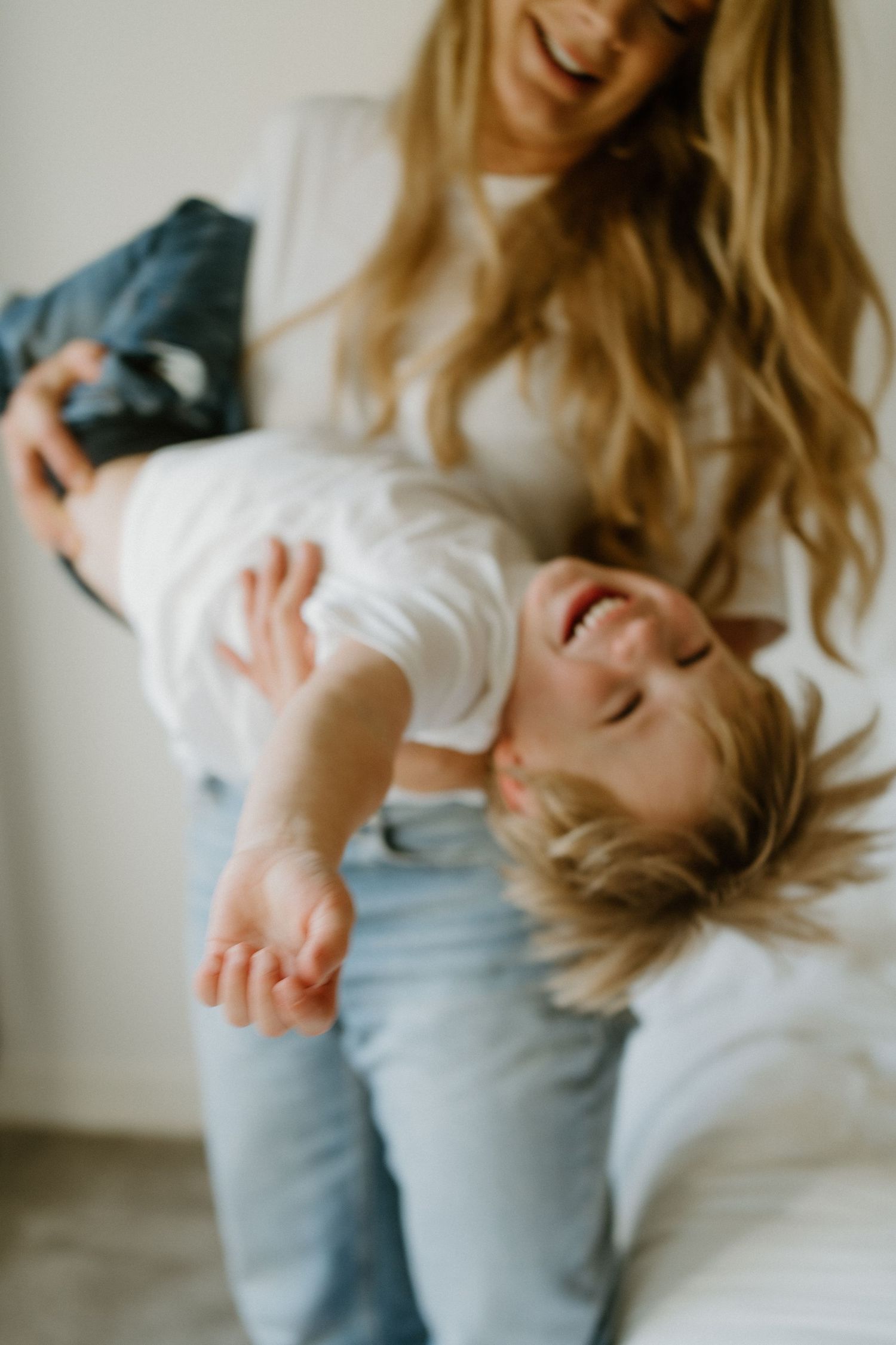 Laughing toddler being playfully held upside down by his smiling blonde mother.