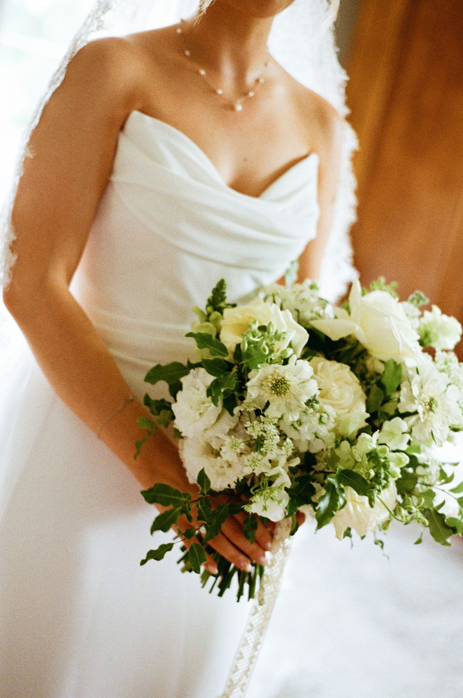 Bride in a strapless white gown holds a lush bouquet of white flowers and greenery.
