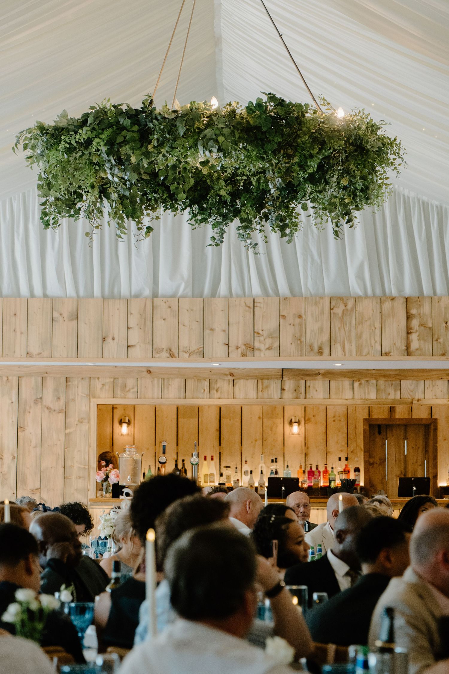 Elegant wedding reception venue with a stunning greenery chandelier hanging above guests seated at tables.