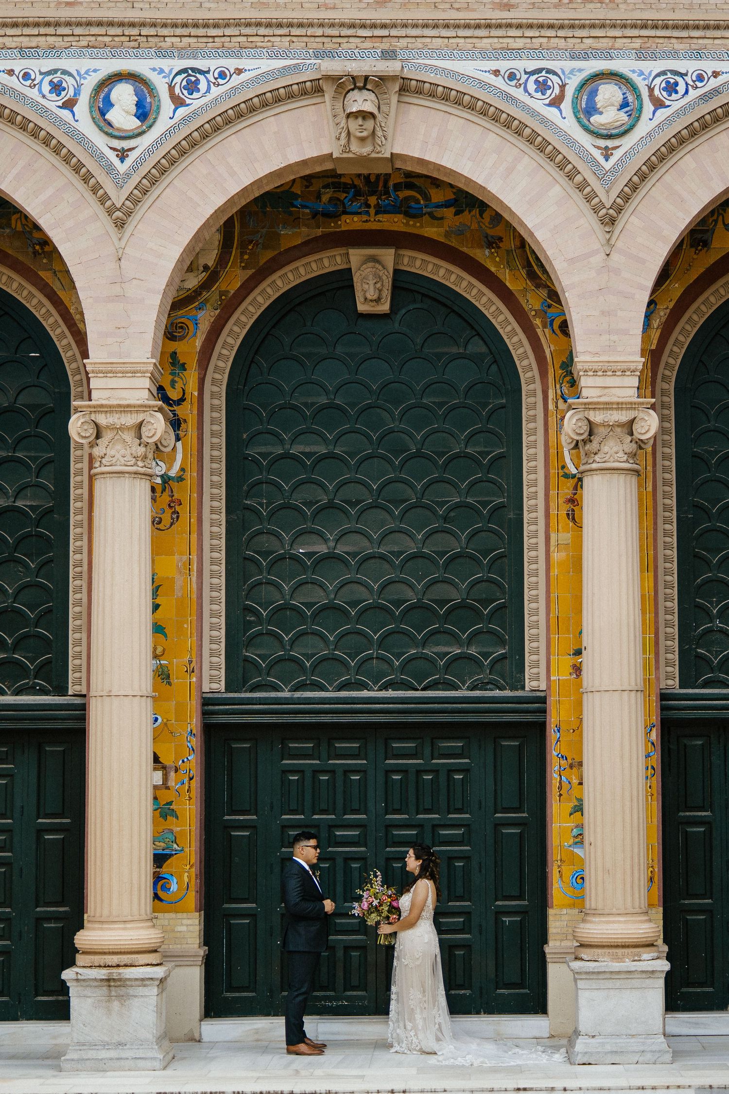 Bride and groom standing together beneath ornate arched doorways with decorative green and gold tilework.