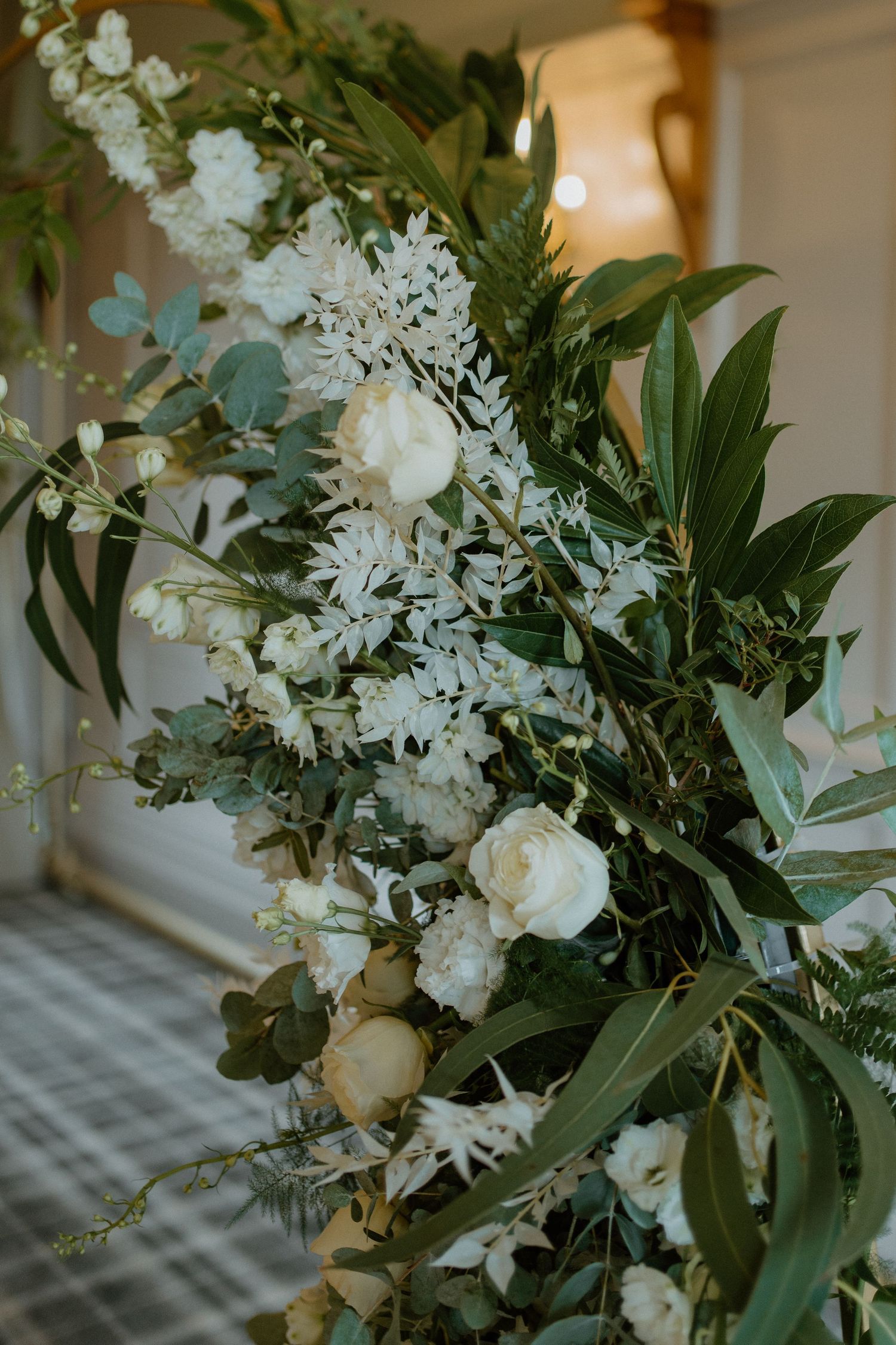 Close-up of lush white roses and greenery floral arch arrangement for wedding ceremony.