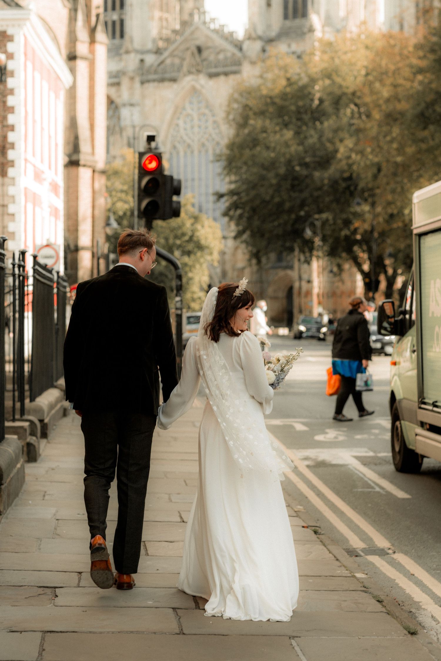 Newlyweds walking down a city street with historic cathedral visible in background.