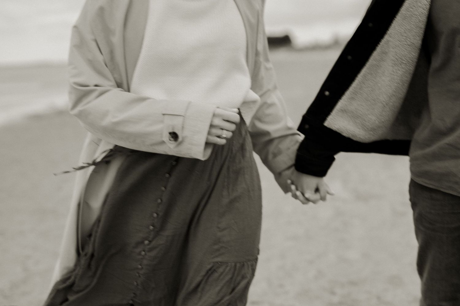 A black and white close-up shot of two people holding hands while walking together.