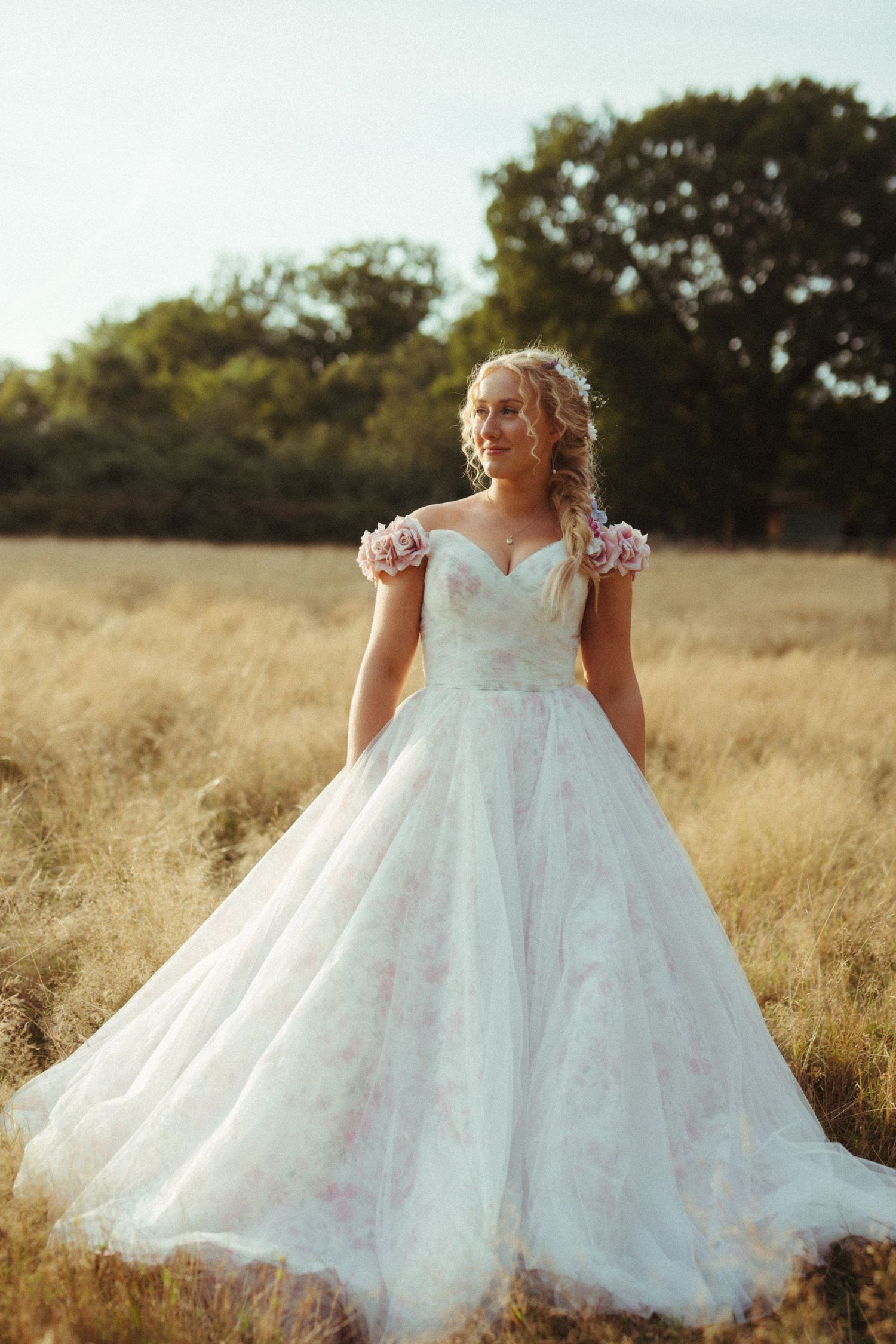 Elegant white wedding dress with floral cap sleeves and full tulle skirt photographed in golden field at sunset.