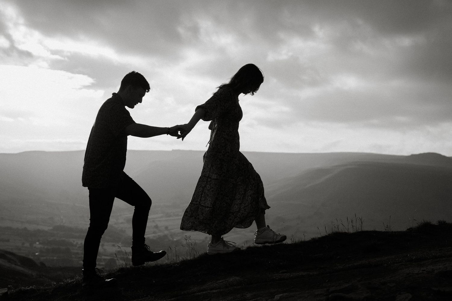 Silhouette of a couple holding hands on a hilltop with dramatic cloudy sky backdrop.