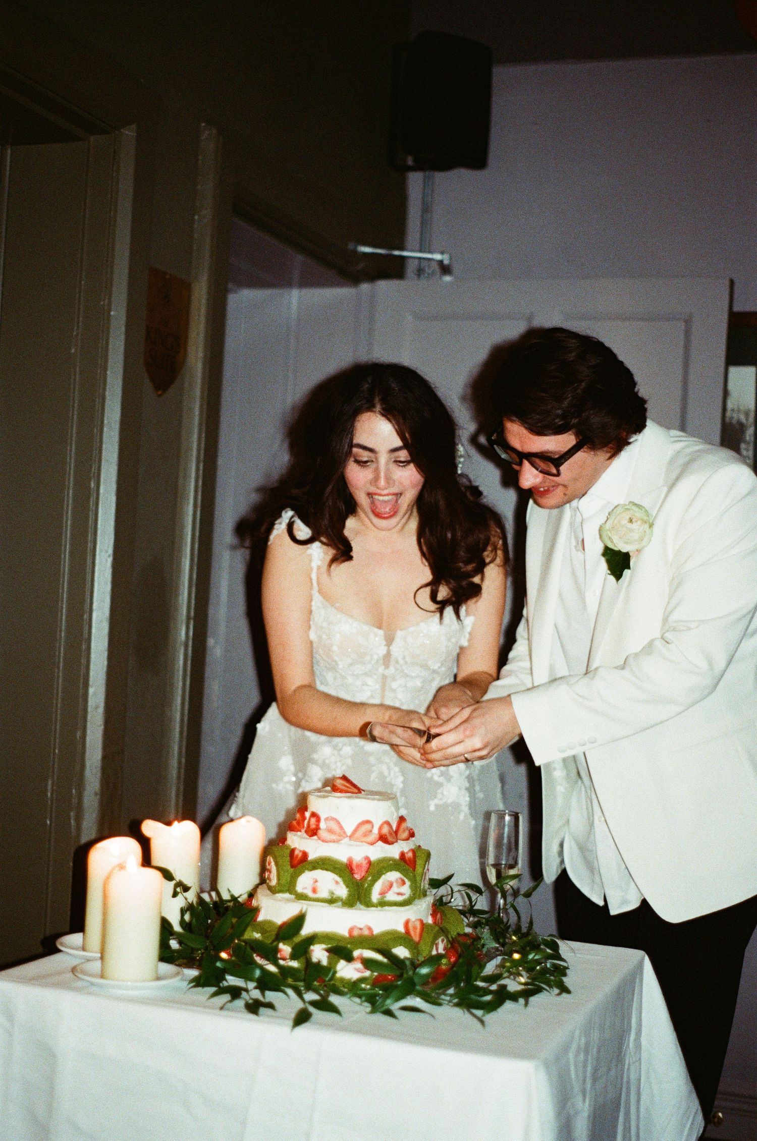 Bride and groom cutting a decorated wedding cake together surrounded by candles and greenery.