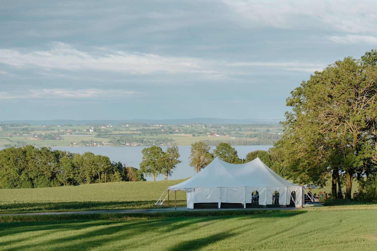 Scenic outdoor wedding tent venue overlooking a river and green countryside landscape.