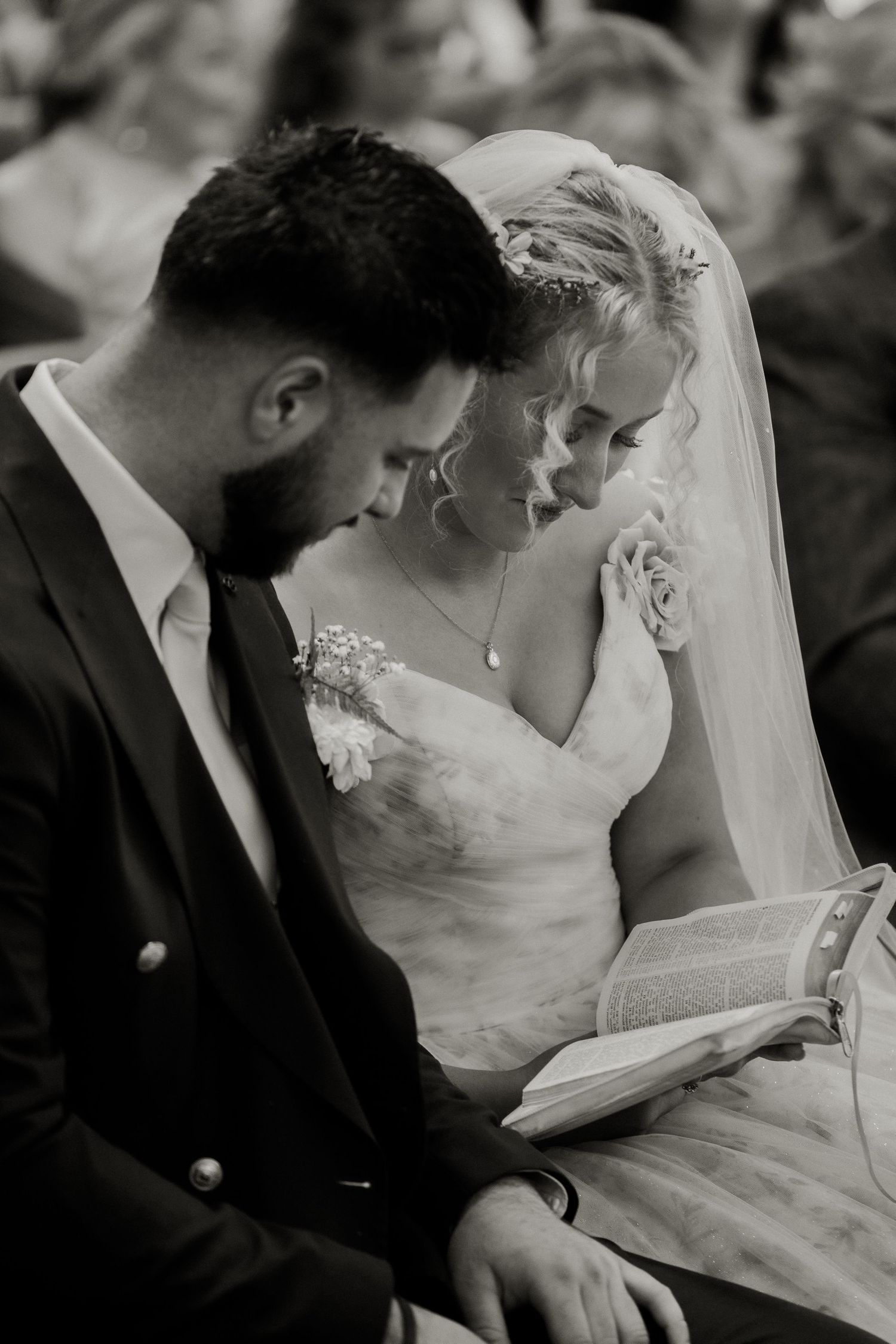 Black and white intimate photo of bride and groom reading from a book together during ceremony.