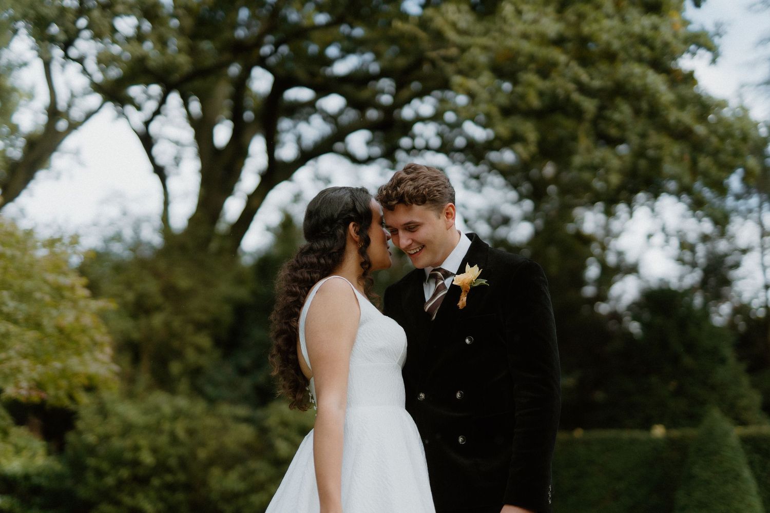 A bride and groom share a tender forehead touch in a lush green garden on their wedding day.