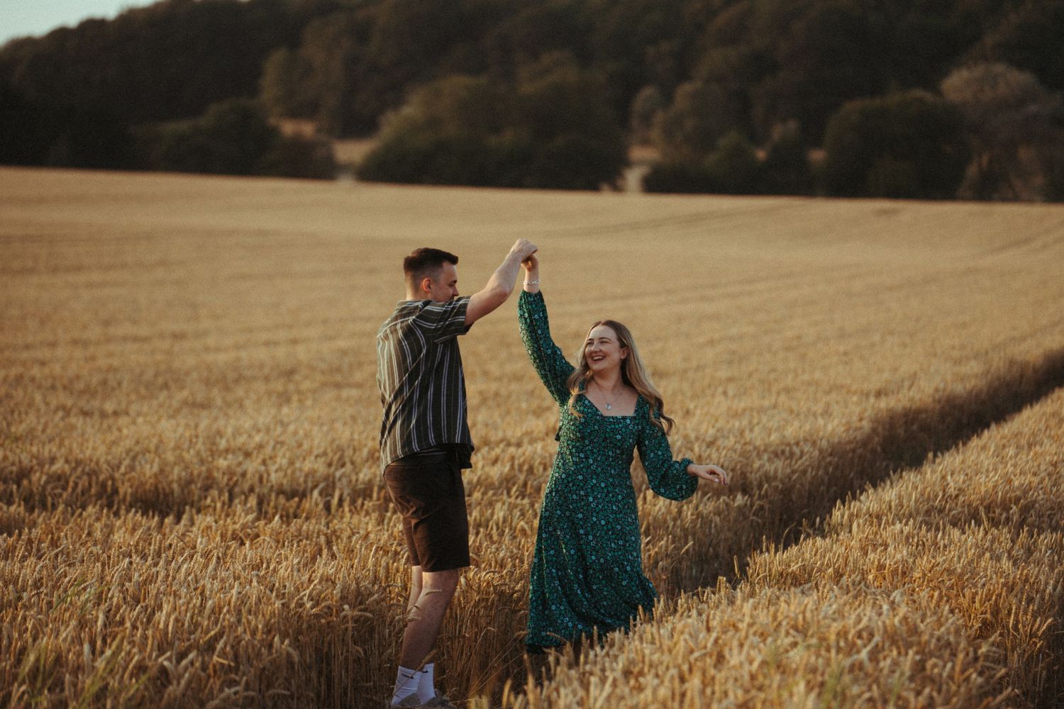 A couple dances together in a golden wheat field at sunset, sharing a joyful moment in nature.