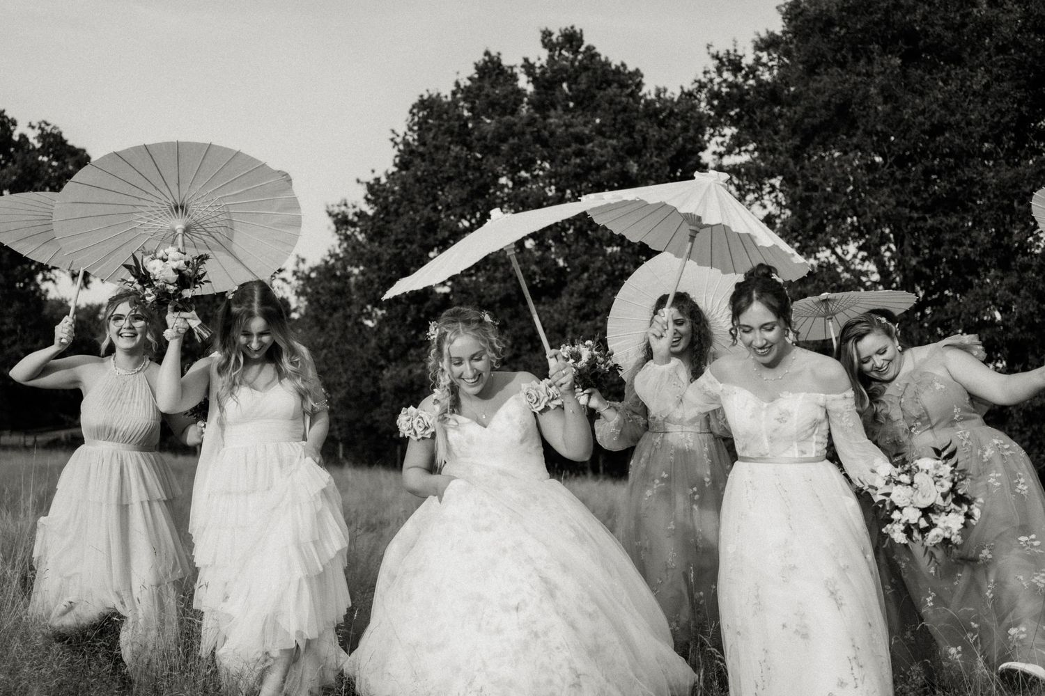 A vintage black and white photograph shows a group in formal white dresses holding parasols outdoors.