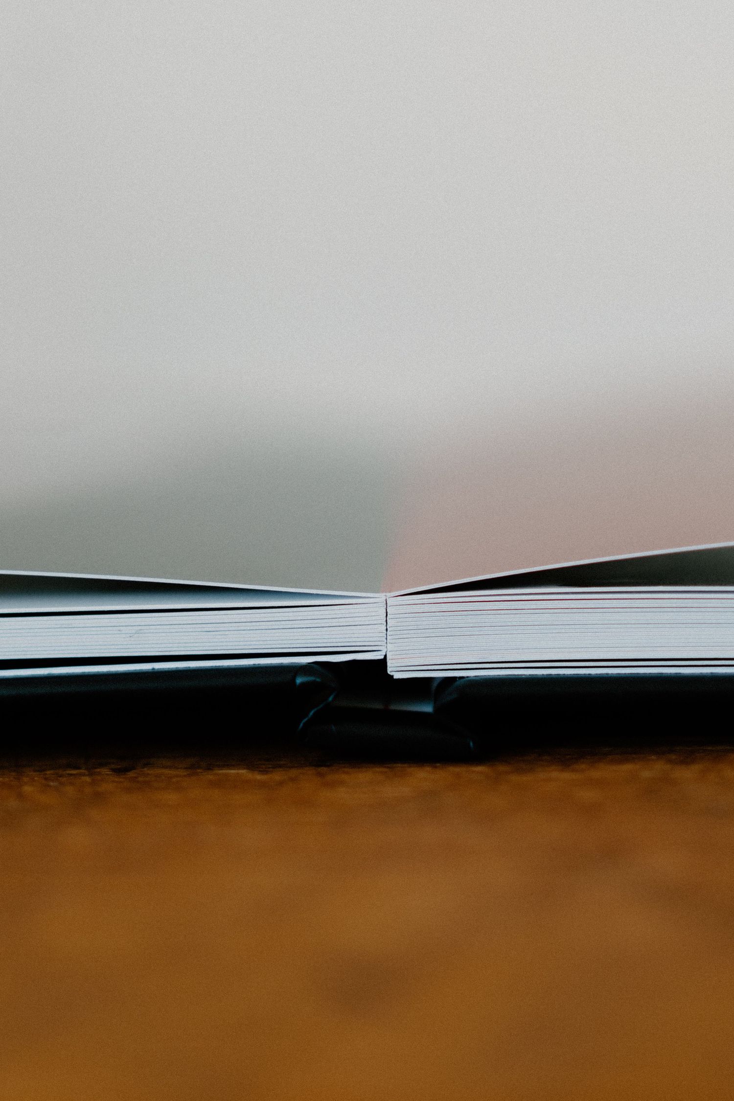 Close-up view of an open book spine against a blurred brown background, showing white paper pages spread apart.