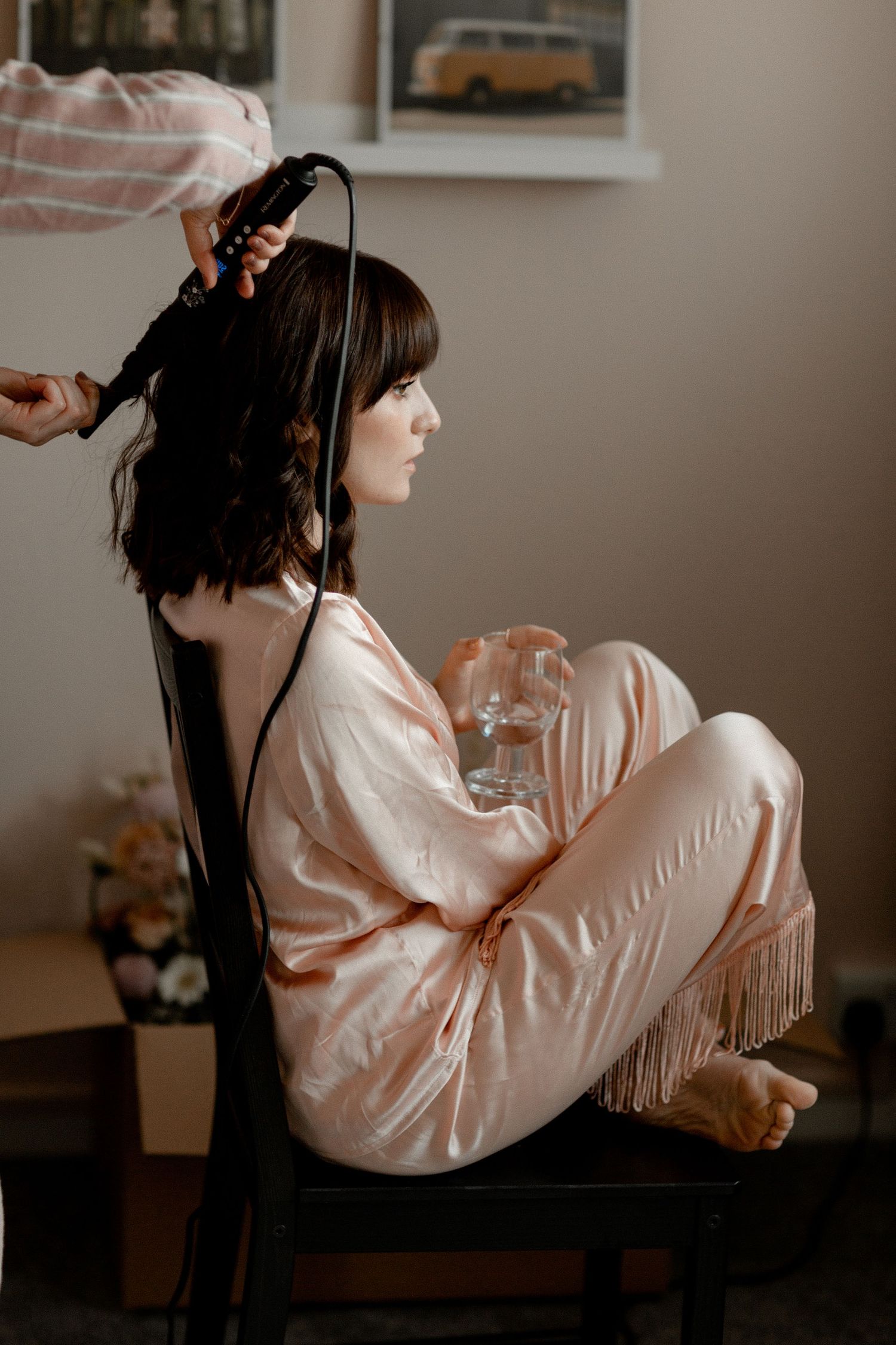 Someone wearing a silk robe sits while getting their hair styled with vintage decor in background.