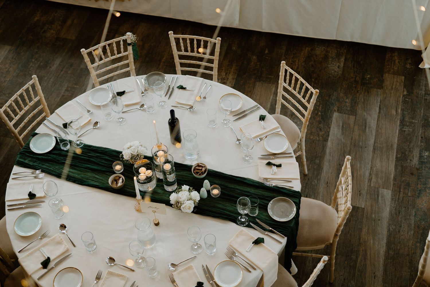 Elegant wedding reception table with green runner, candles, and gold chiavari chairs overhead view.