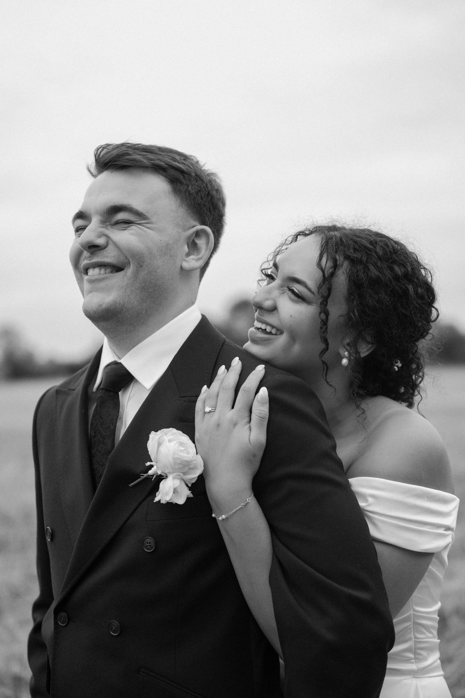 Black and white portrait of smiling bride and groom embracing outdoors in an open field.