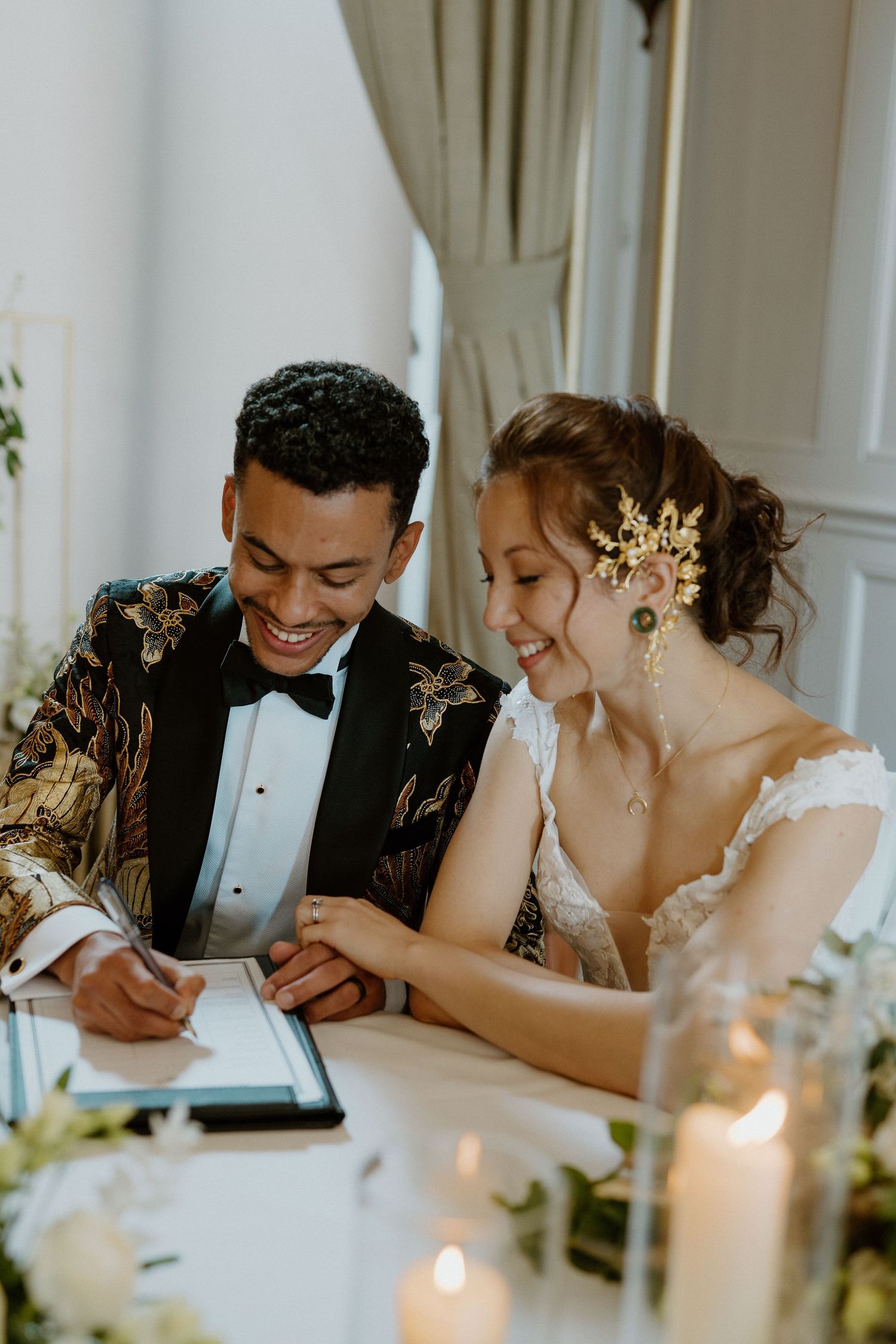 Bride and groom laughing while signing wedding register at candlelit table.