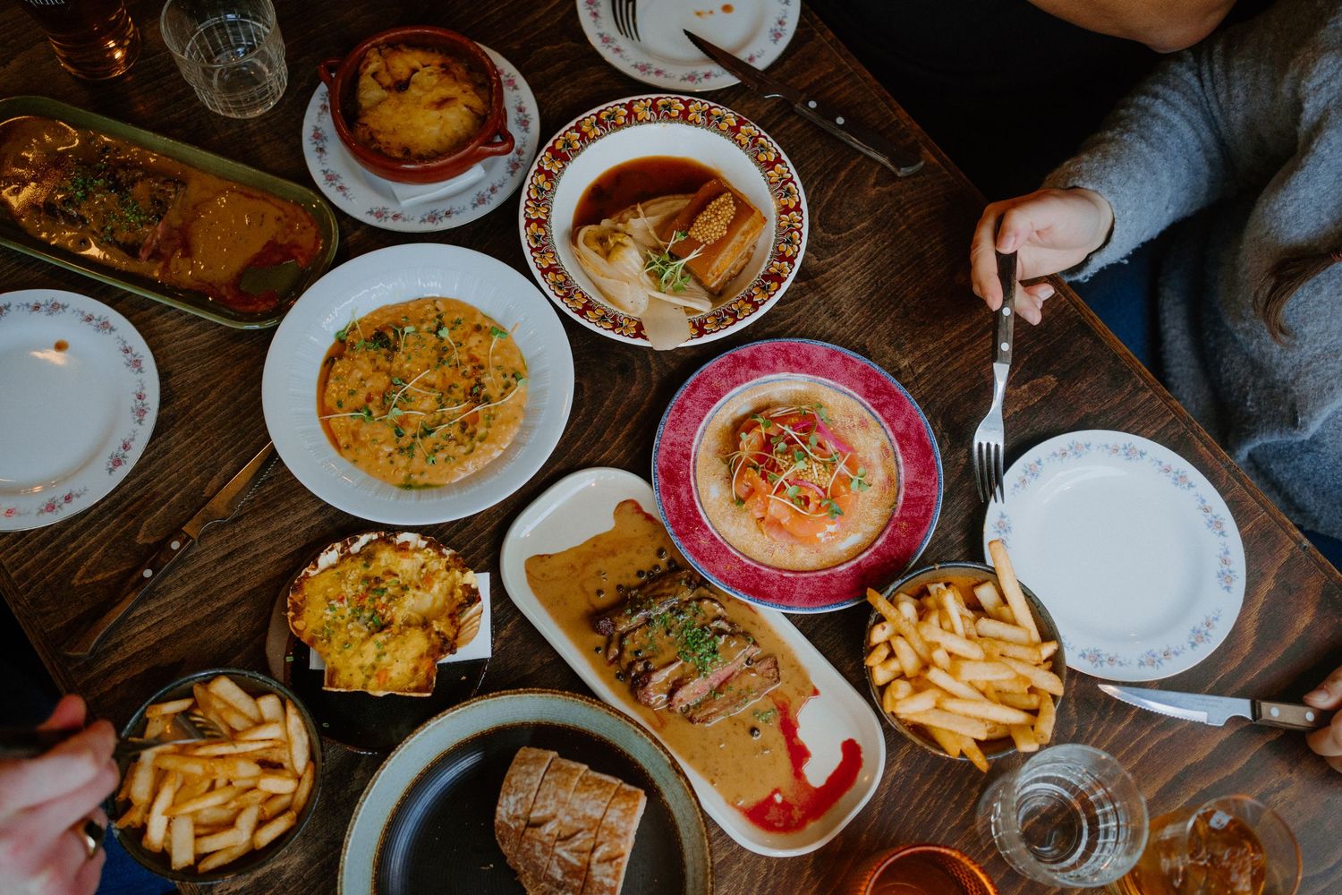 Overhead view of casual restaurant dining spread with french fries, soups, sandwiches and various dishes on wooden table.