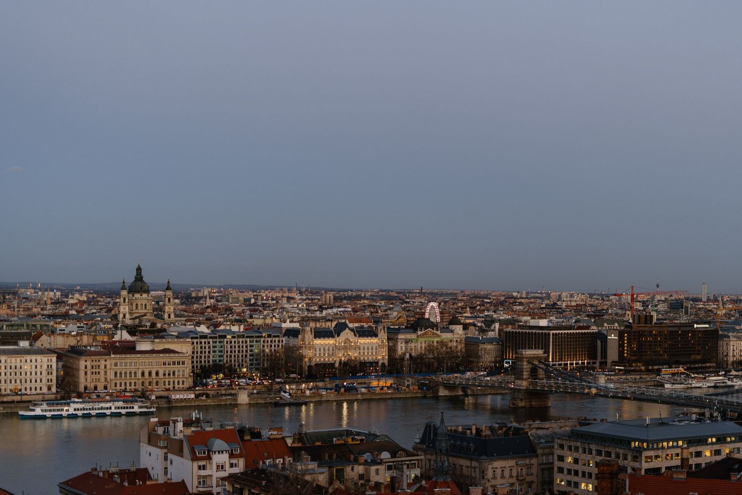 Panoramic sunset view of Budapest's historic cityscape along the Danube River with ornate architecture and buildings.