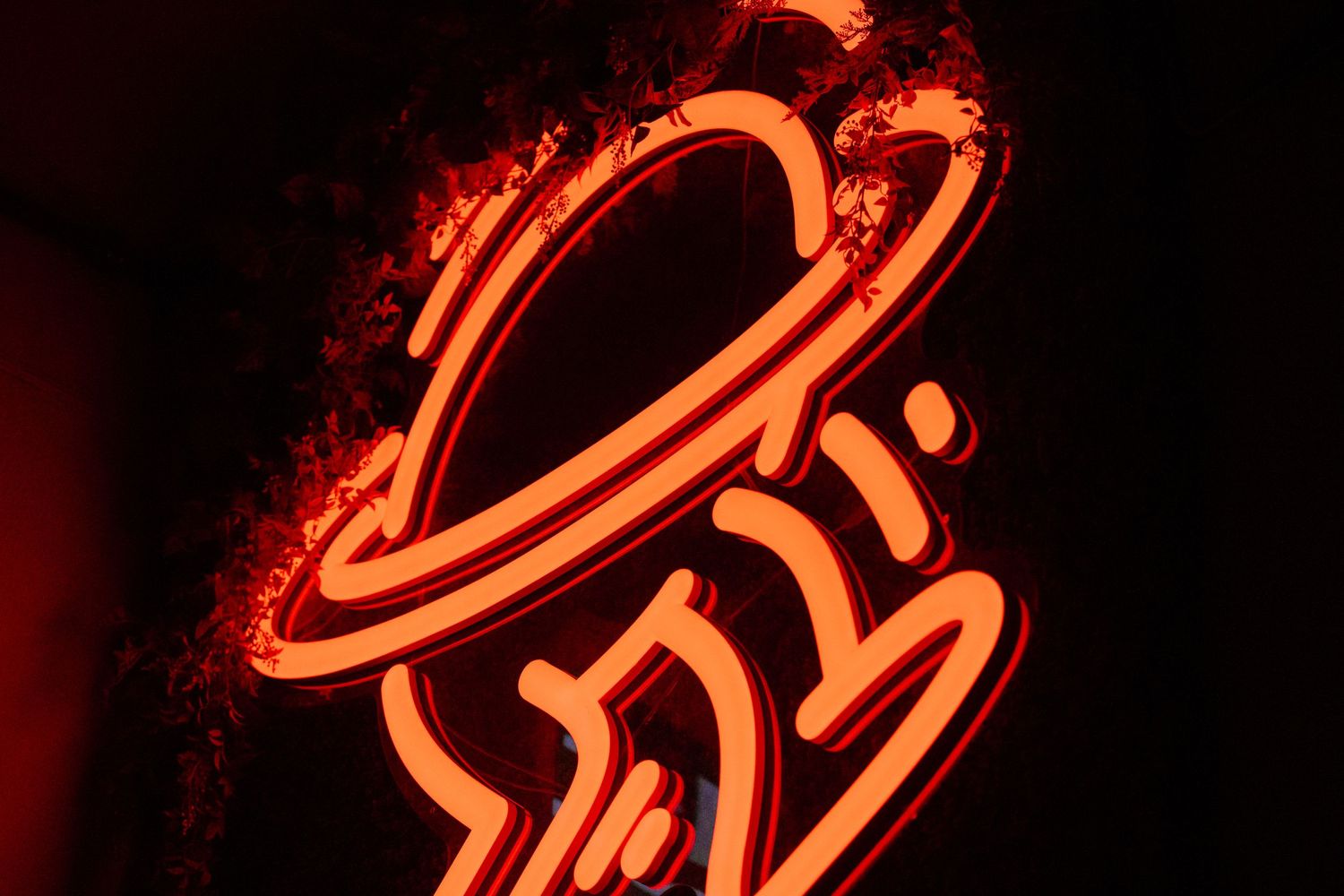 Neon orange sign showing a stylized hat or UFO shape glowing against dark background.