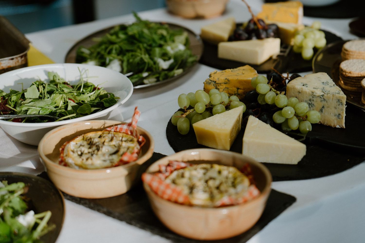A spread of appetizers with cheese board, green salad plates, and copper bowls filled with dips.