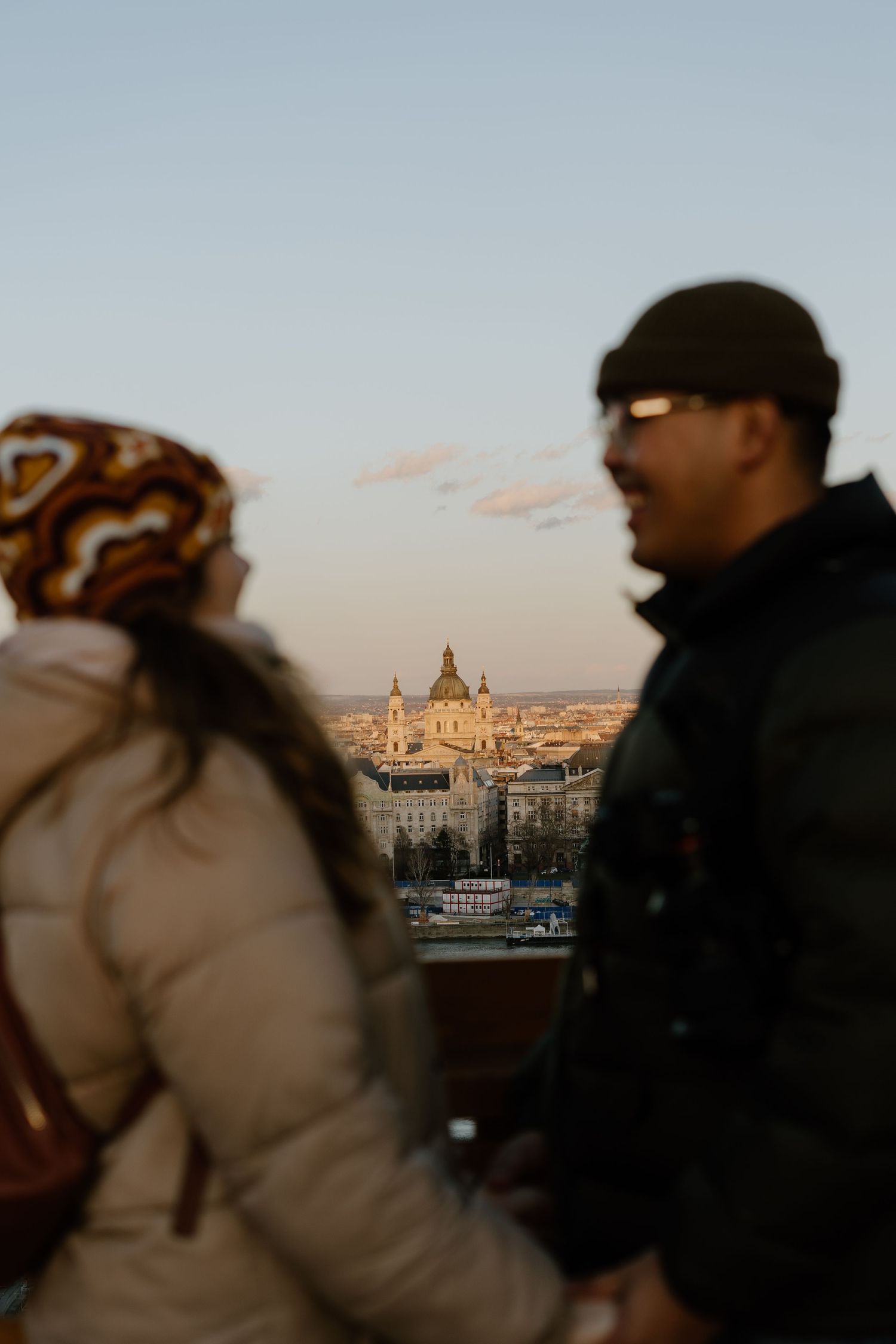 Two people viewing the cityscape of Budapest at dusk with Saint Stephen's Basilica dome visible in the background.