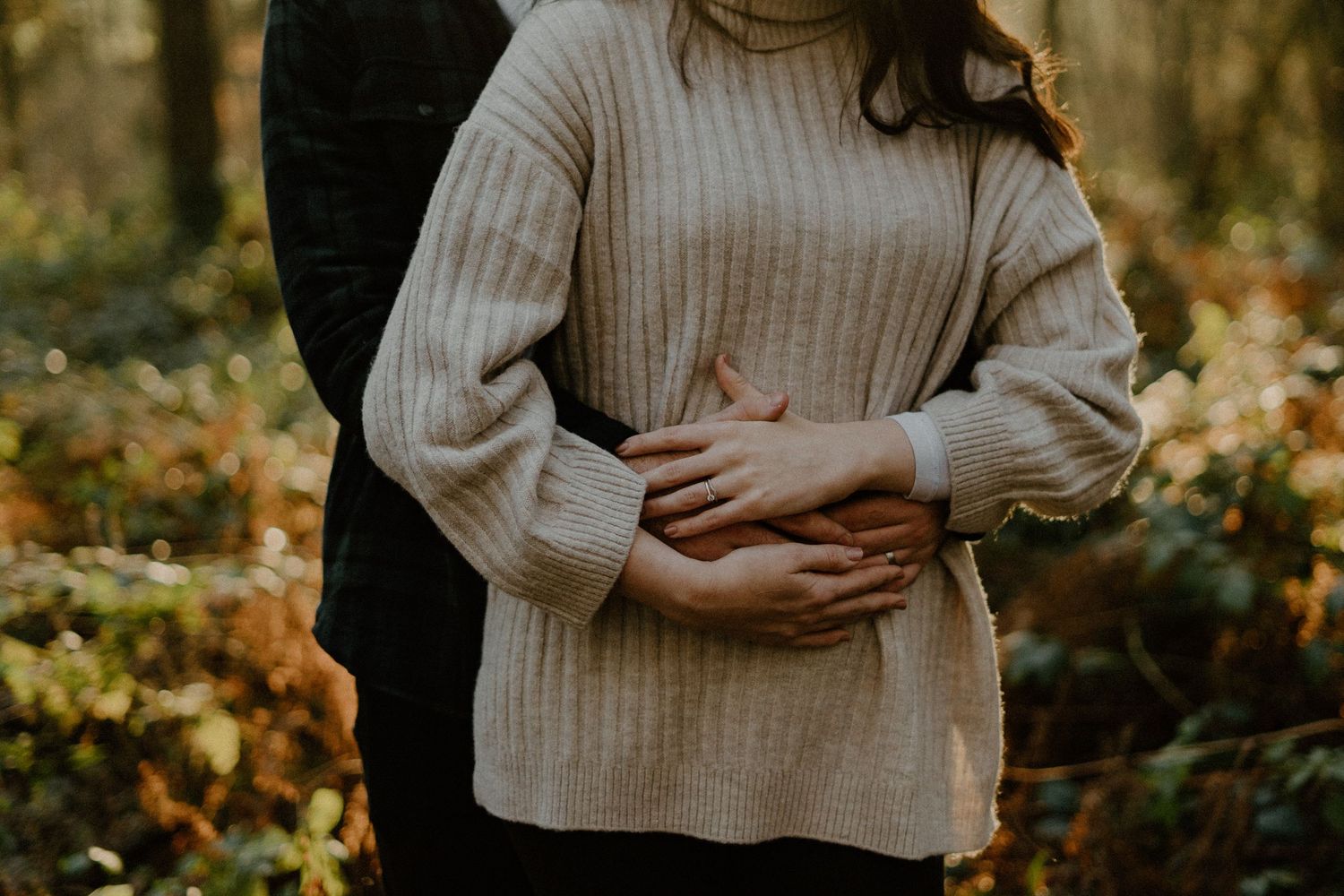 Close-up of couple holding hands on pregnant belly in autumn forest, maternity photo.