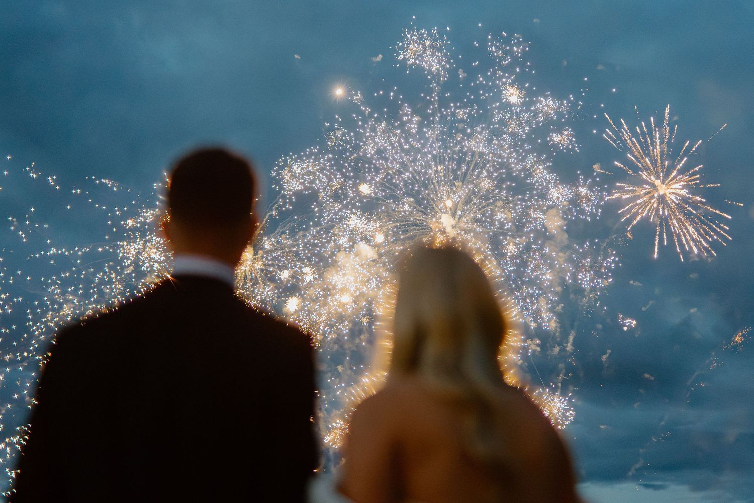 Bride and groom watching a spectacular fireworks display lighting up the evening sky together.