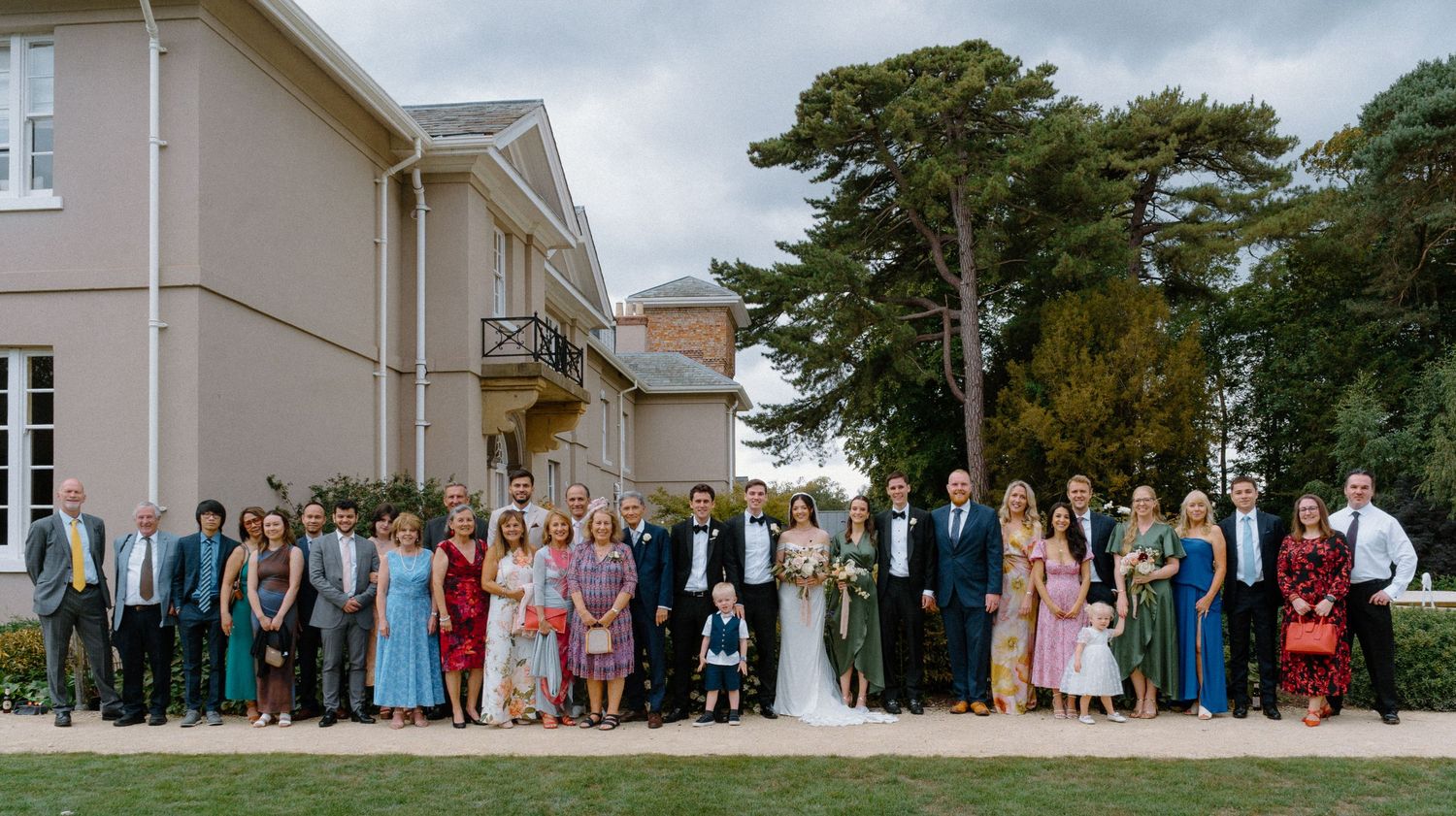 Large wedding group photo of all guests and wedding party on lawn outside elegant manor house.