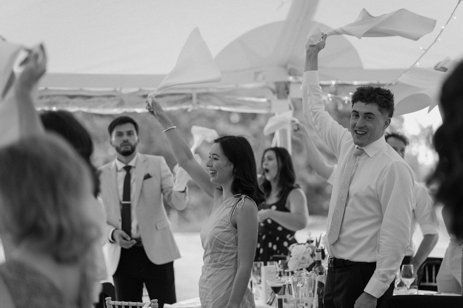 Black and white photo of wedding guests dancing and celebrating inside a marquee reception tent.
