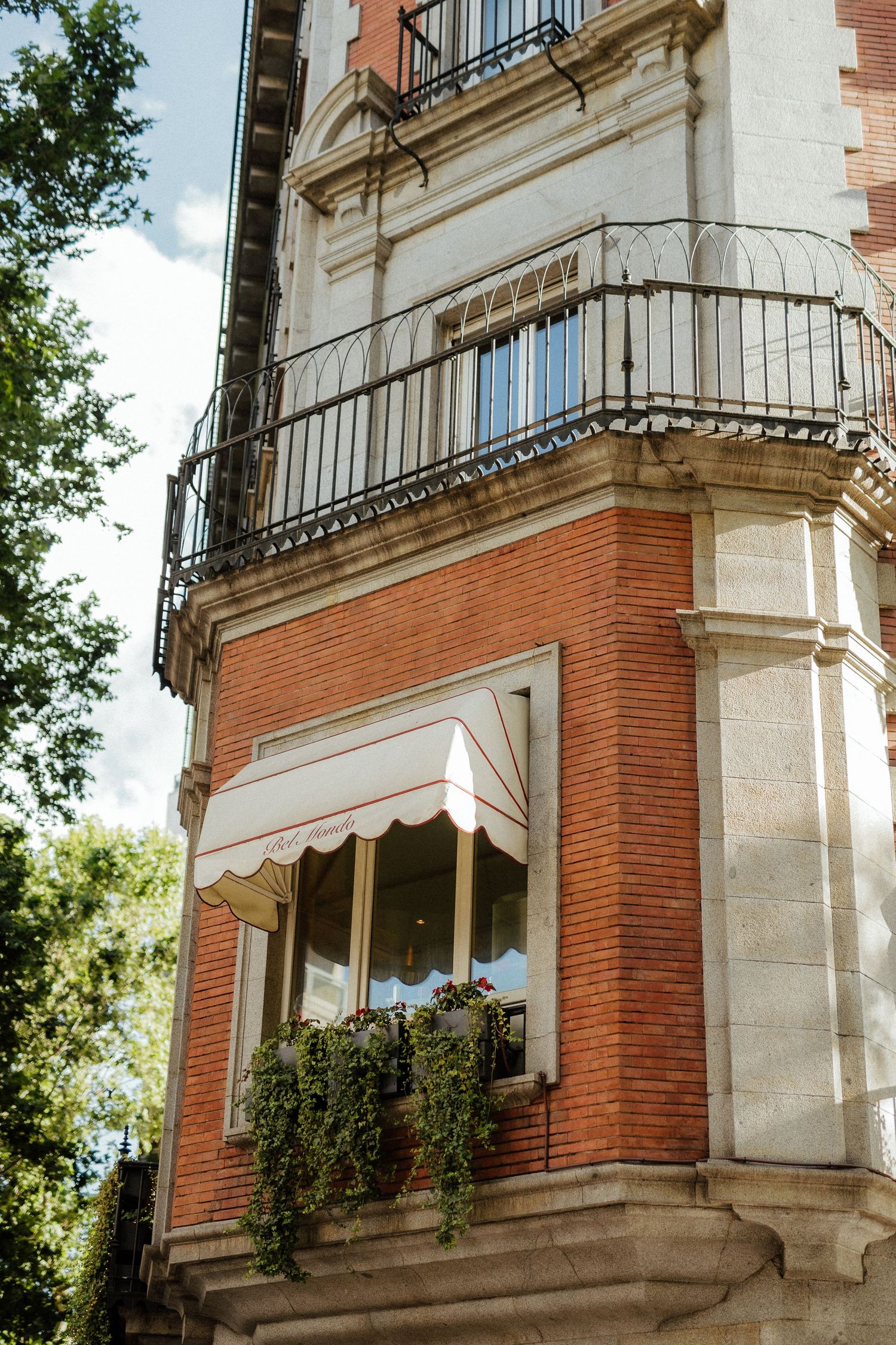 Ornate brick and stone building corner with wrought iron balcony and flower window box.