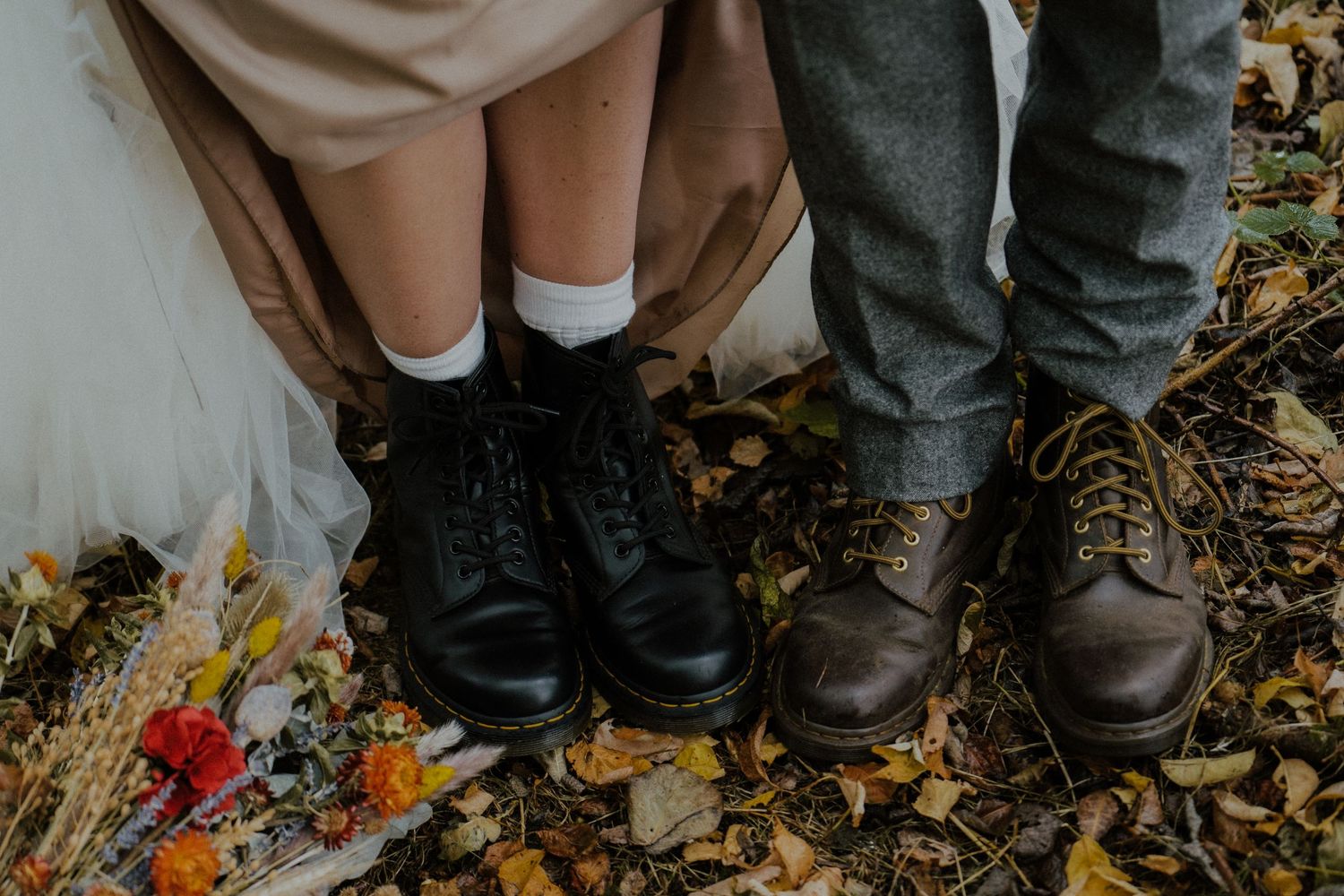 Two pairs of wedding shoes with black and brown leather standing among autumn leaves.