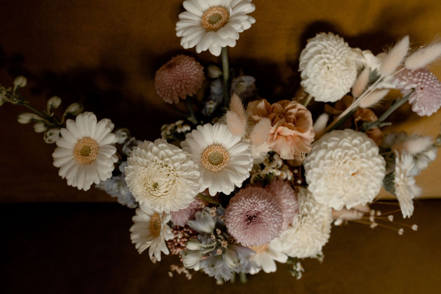 A delicate arrangement of dried white and pink flowers including daisies and other blooms against a dark background.