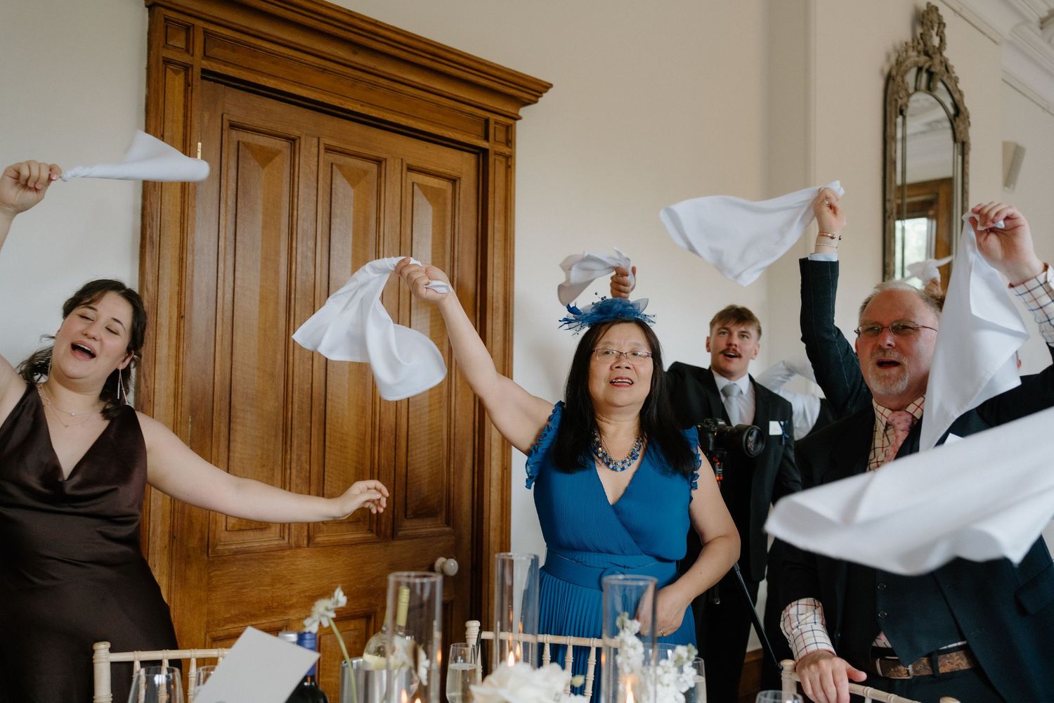 Joyful wedding guests waving white napkins in celebration during a lively wedding reception entrance.