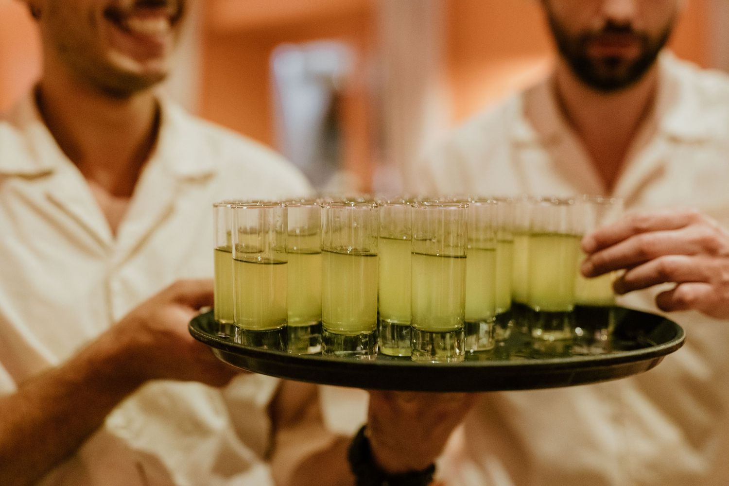 Servers holding a tray of green cocktail shots at a wedding reception.