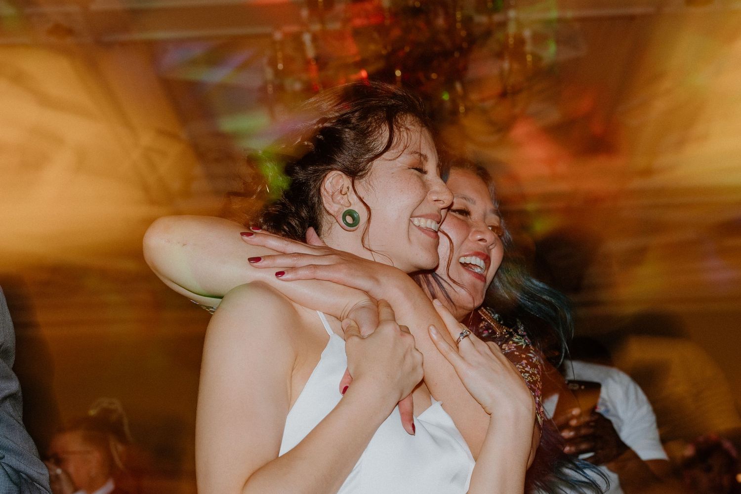 Bride laughing and dancing joyfully with a guest during lively wedding reception celebration.