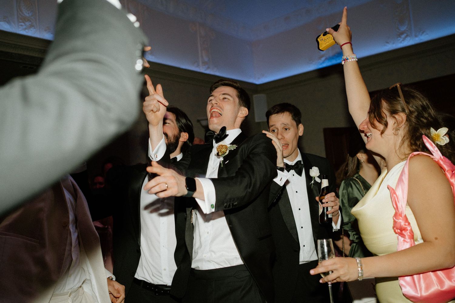 Groom and groomsmen celebrating on dance floor in black tuxedos at lively wedding reception party.